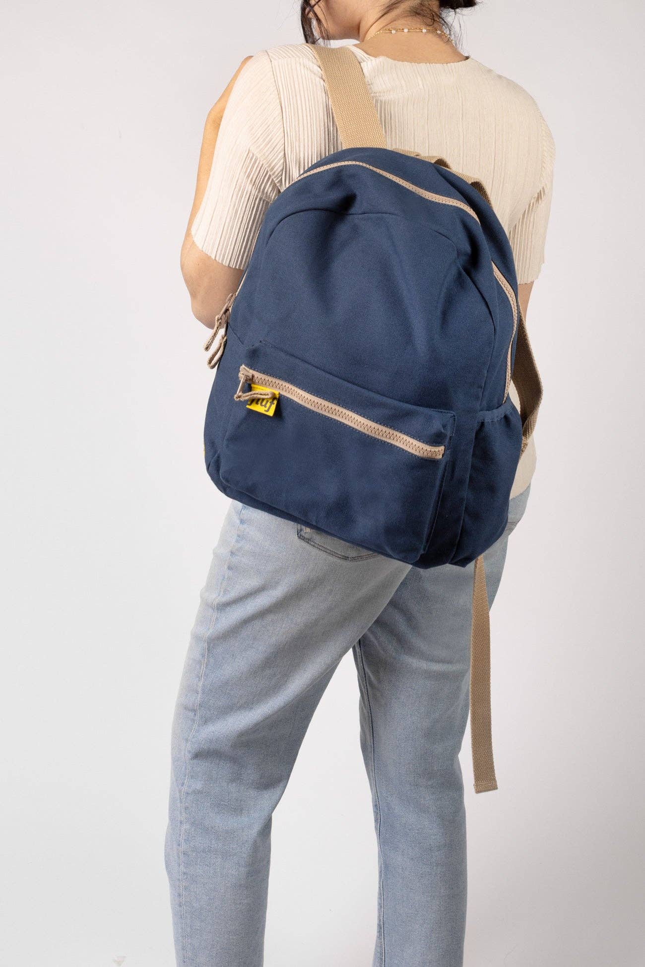 Person wearing a navy blue backpack with beige straps on a plain background