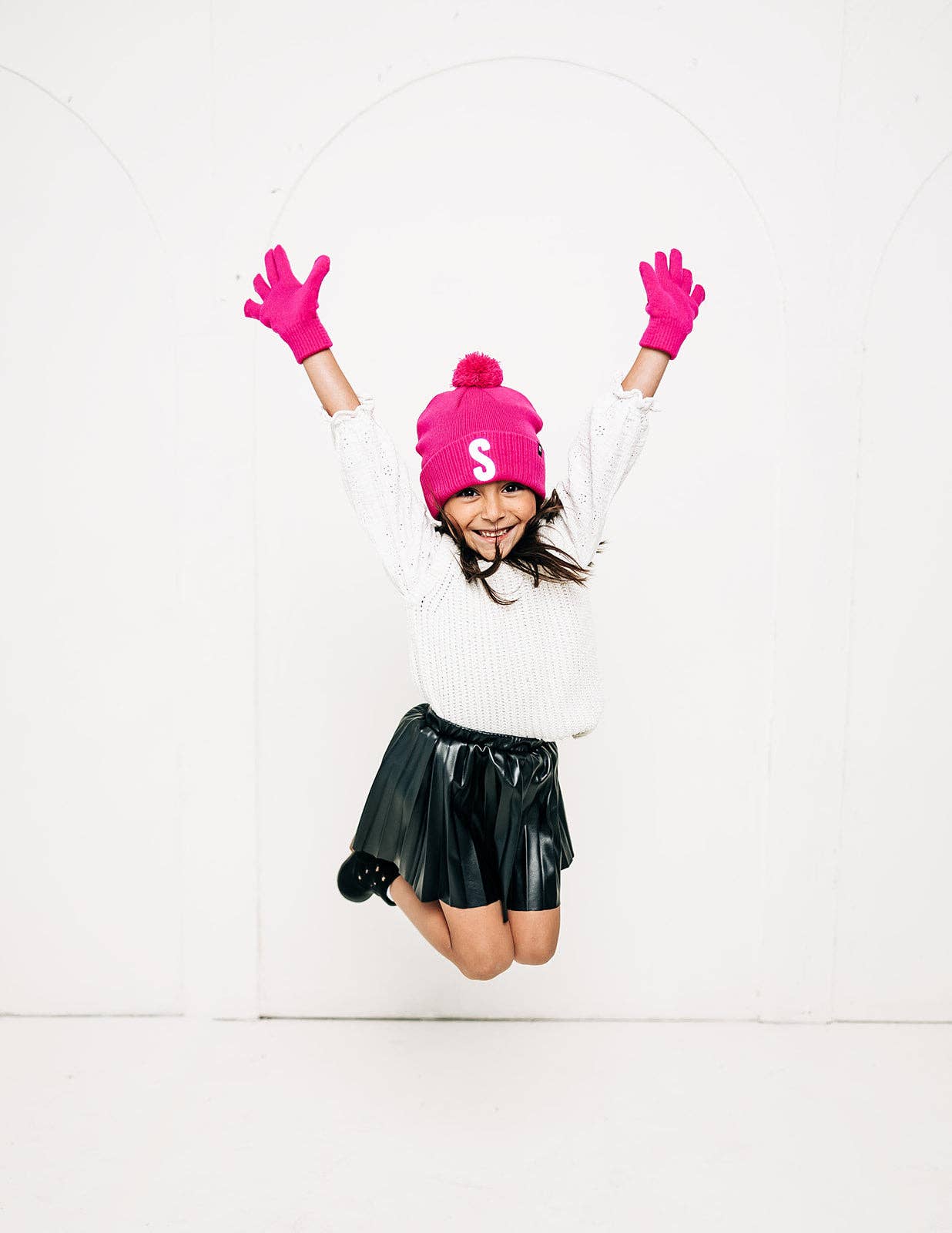 Person wearing a white sweater, black skirt, pink beanie with a letter 'S', and pink gloves on a white background