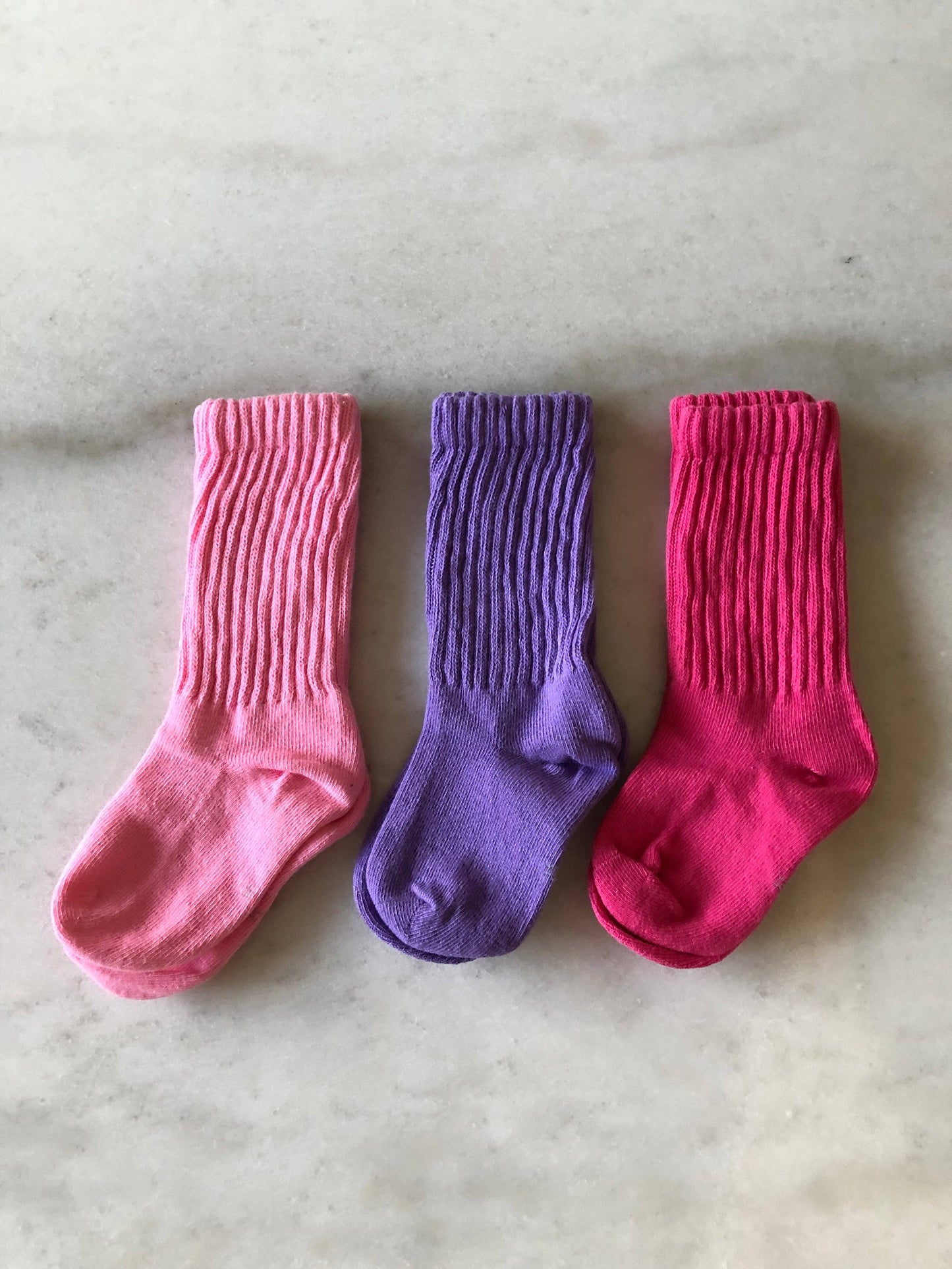 Three pairs of colorful socks (pink, purple, red) on a marble surface.