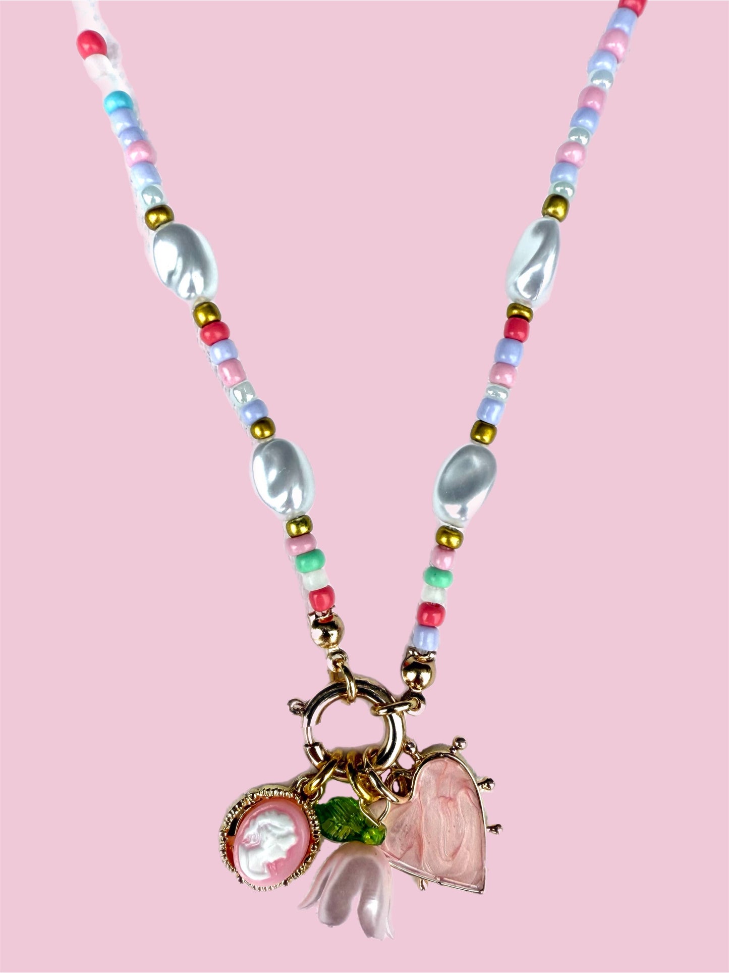 Necklace with colorful beads and heart-shaped pendants on a pink background