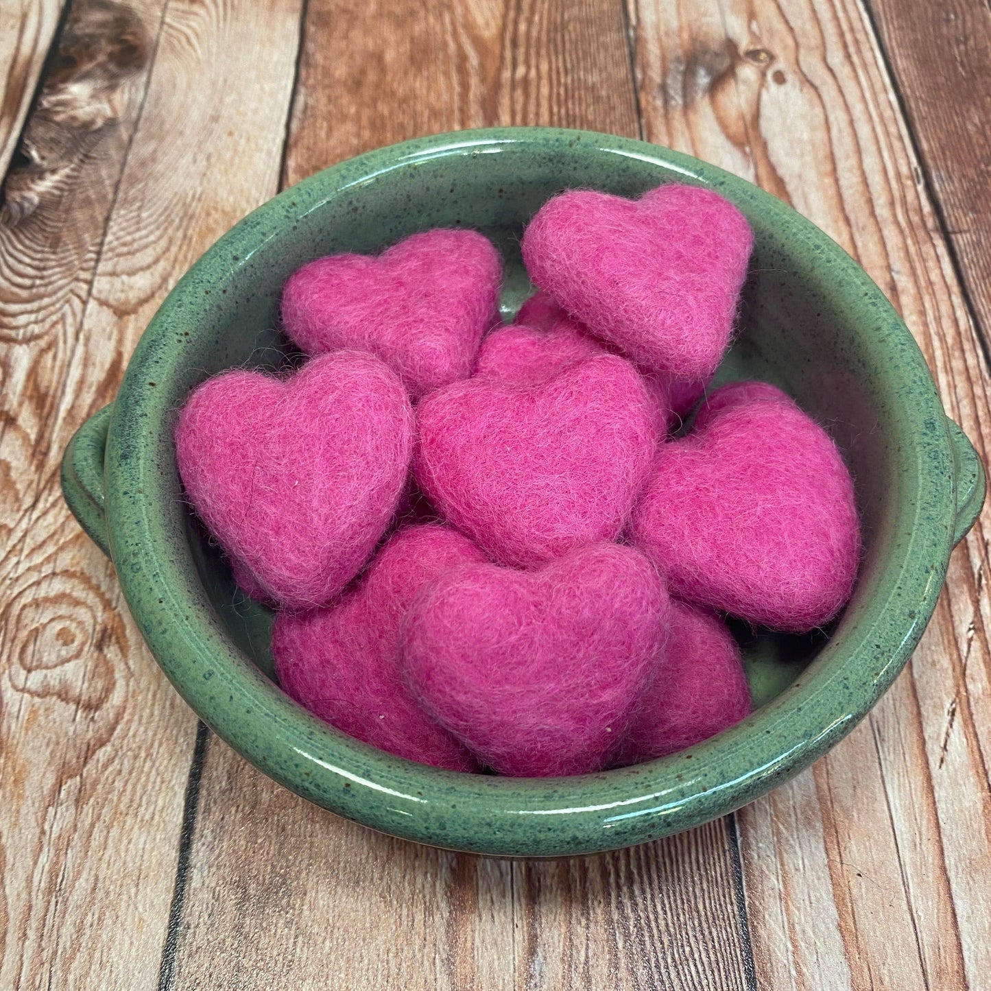 Green bowl filled with pink heart-shaped objects on a wooden surface