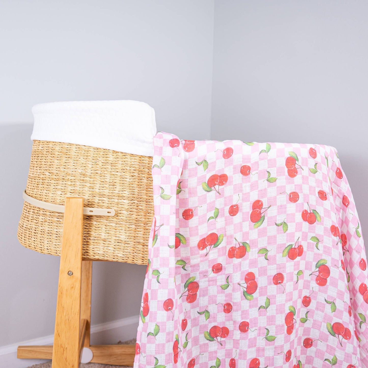 Pink blanket with cherry pattern draped over a wooden chair next to a wicker basket.
