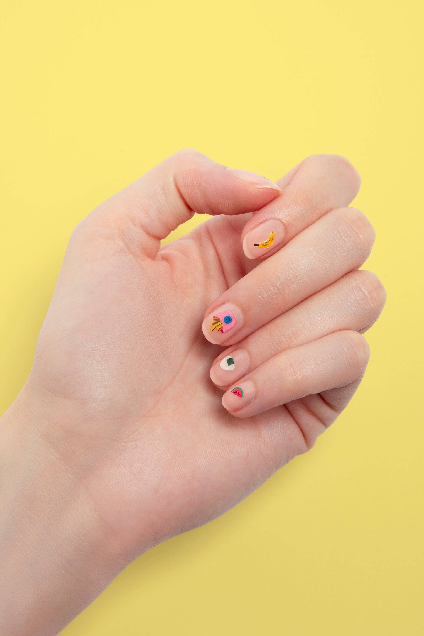 Close-up of a hand with decorated nails against a yellow background