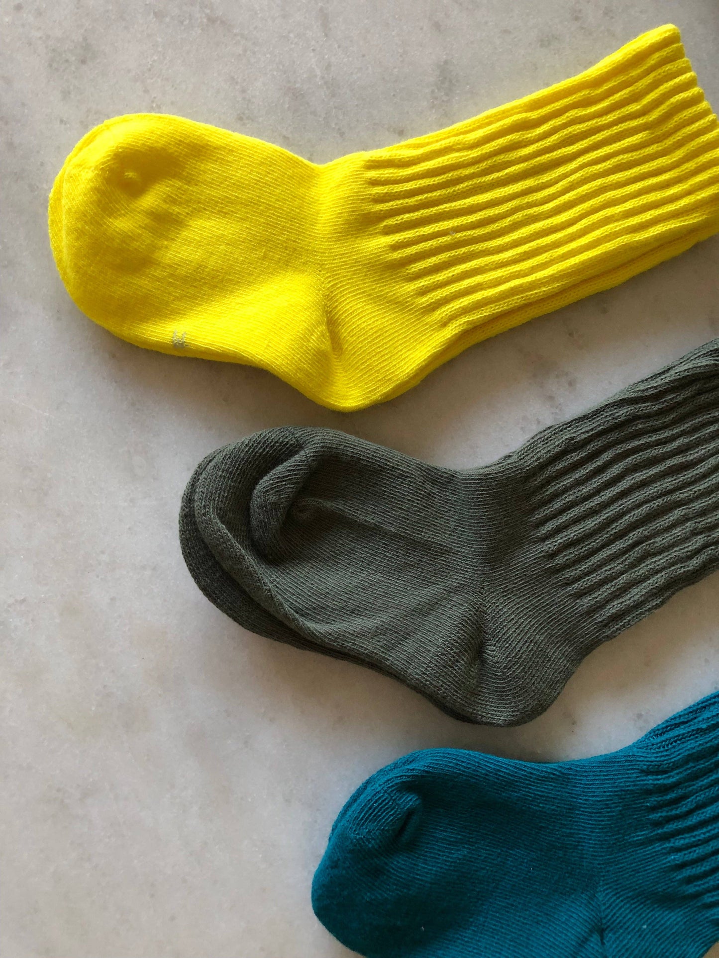 Three socks in yellow, gray, and blue on a light marble surface.