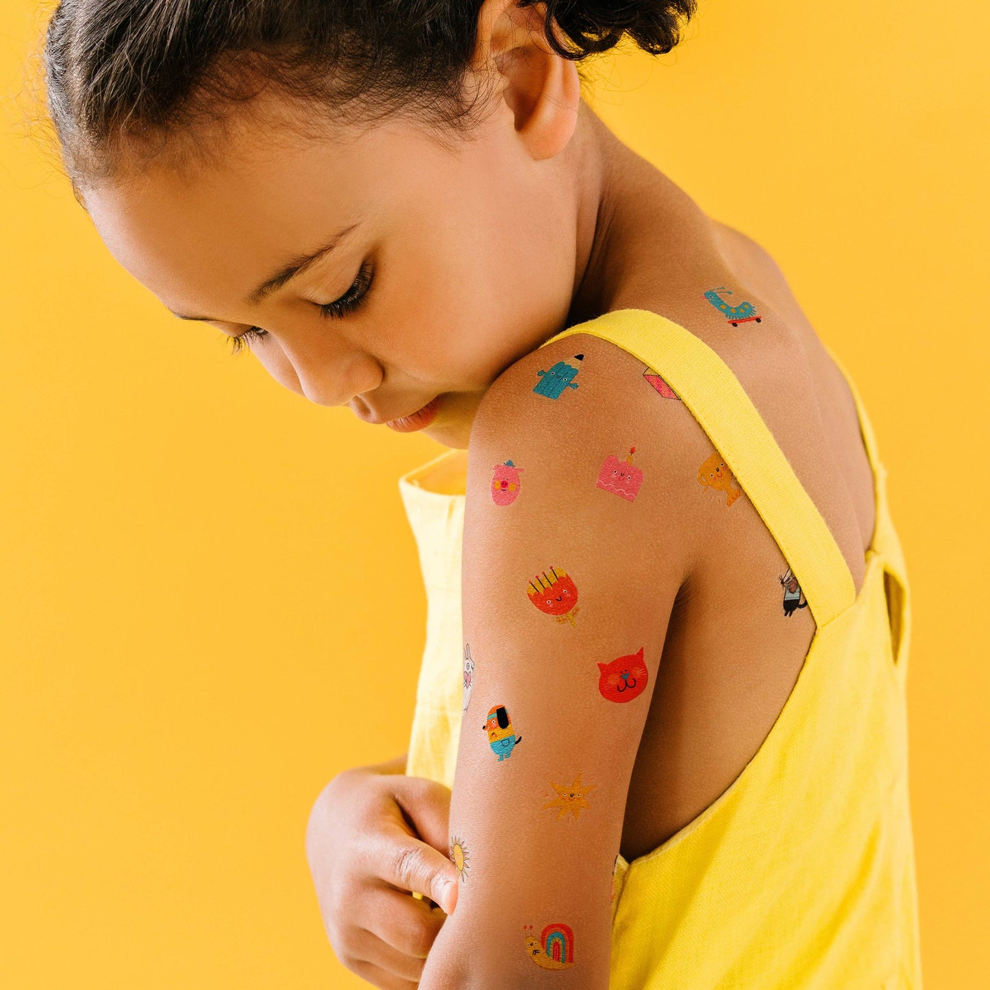 Child with colorful temporary tattoos on a yellow background