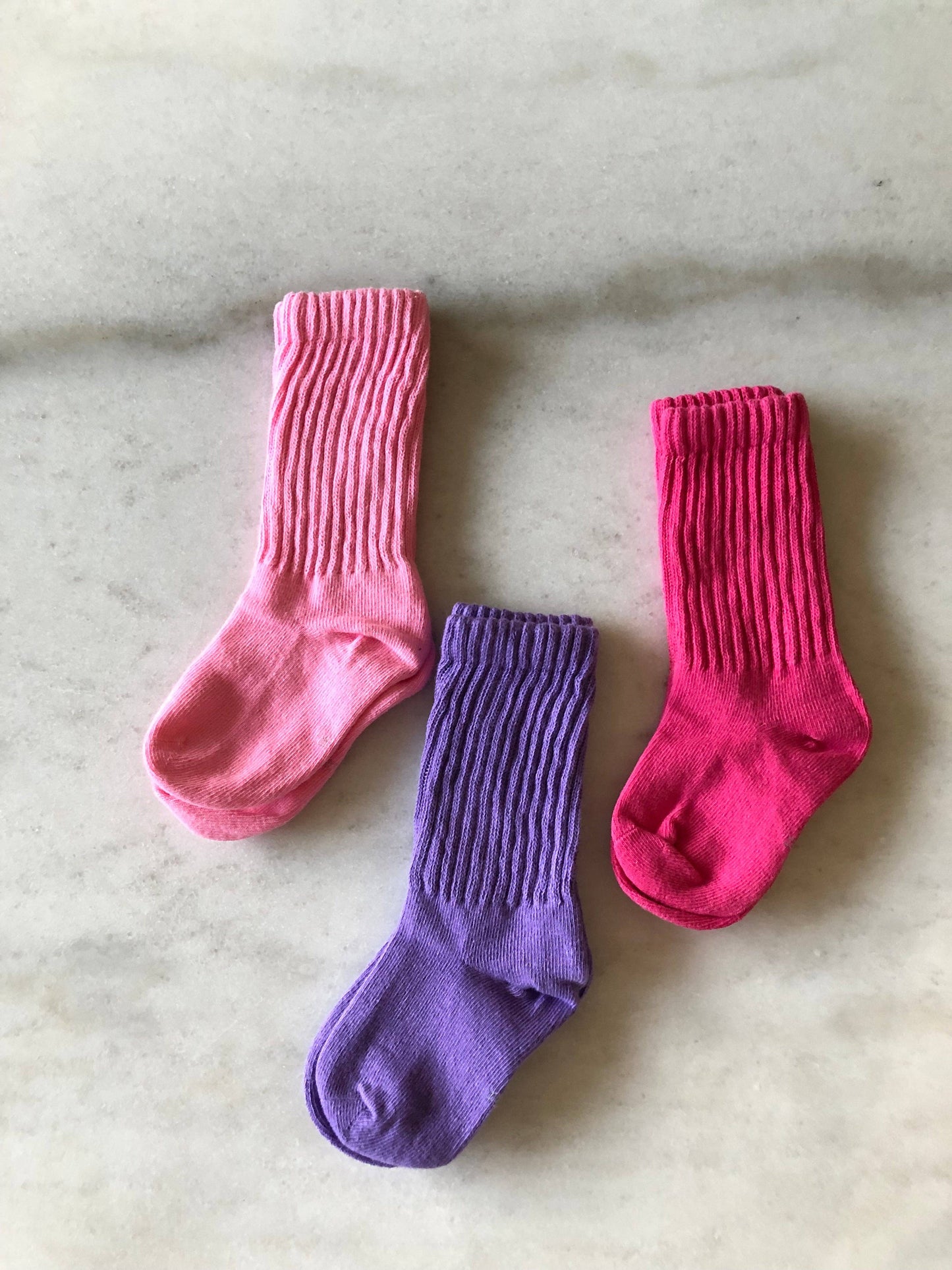 Two pink socks and one purple sock on a marble surface
