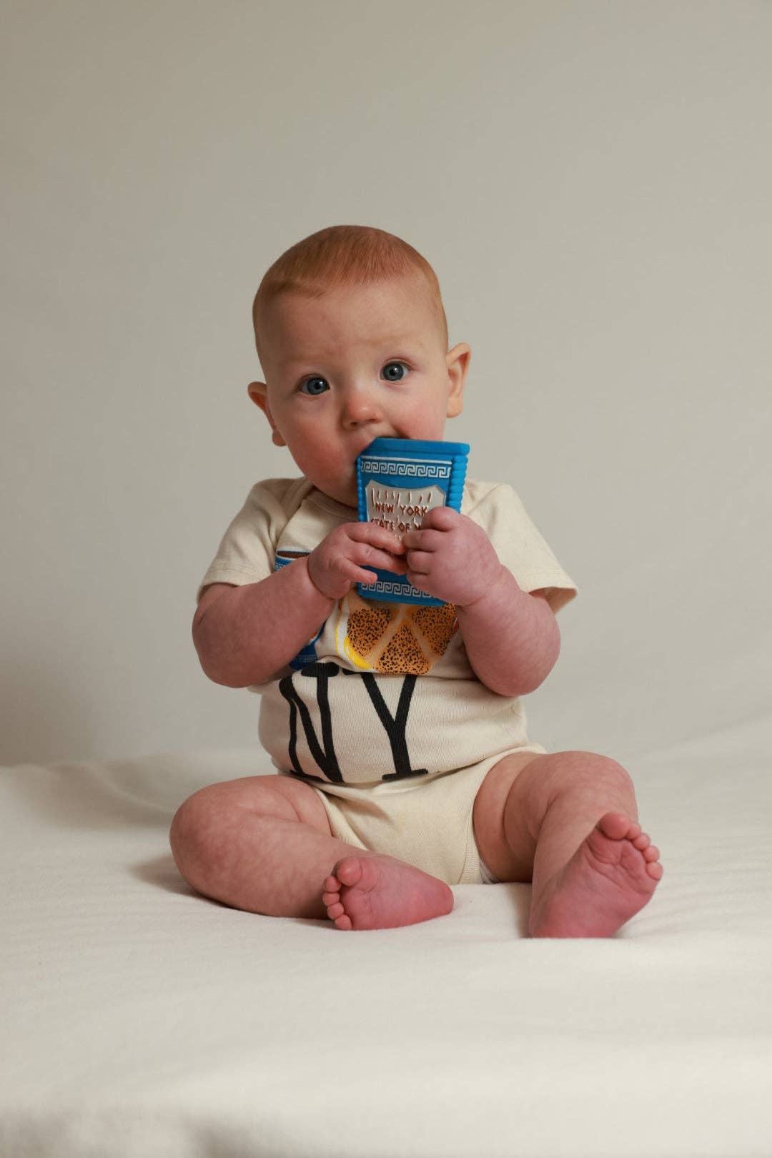 Baby sitting on a white surface holding a blue container.