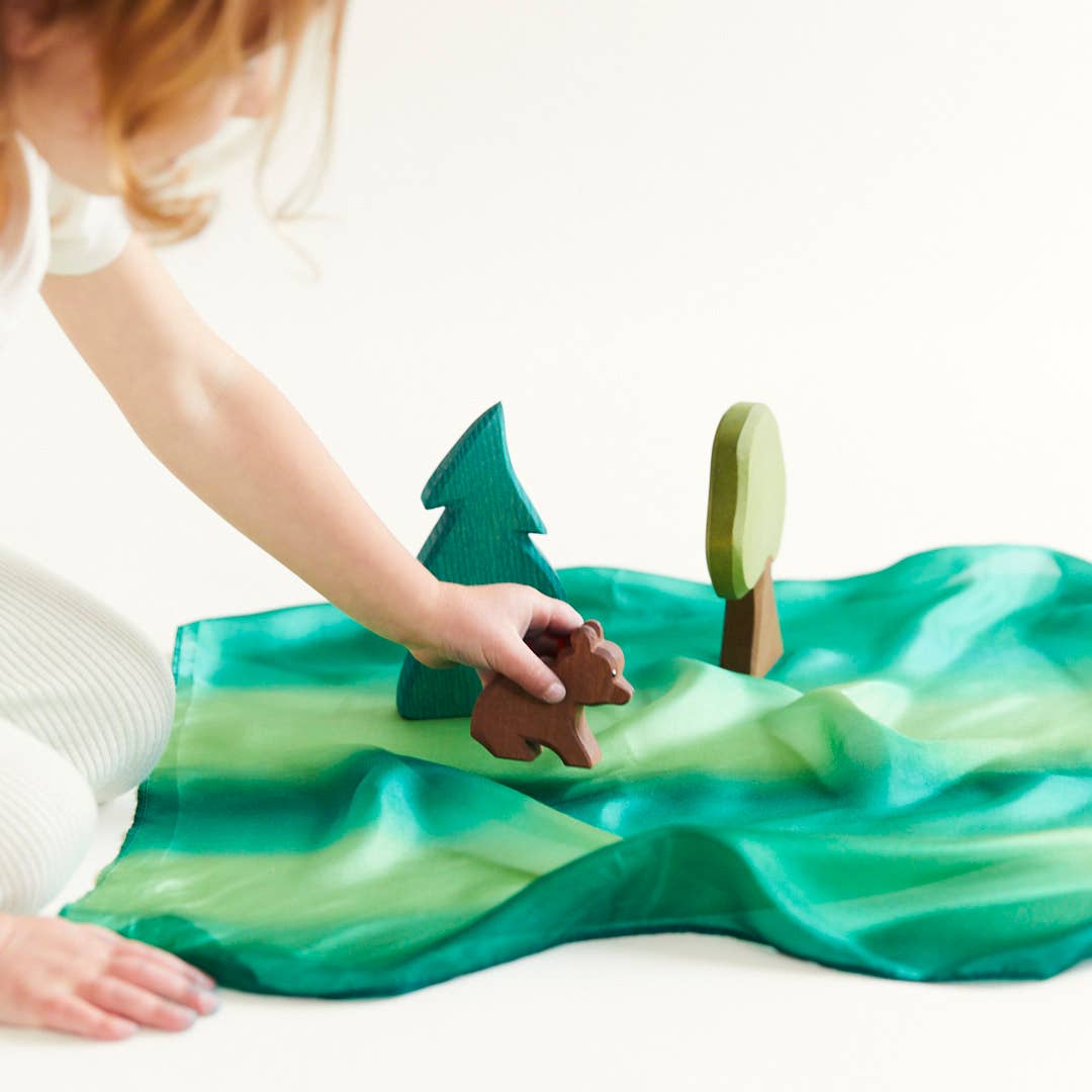 Child playing with wooden bear and tree toys on a green fabric