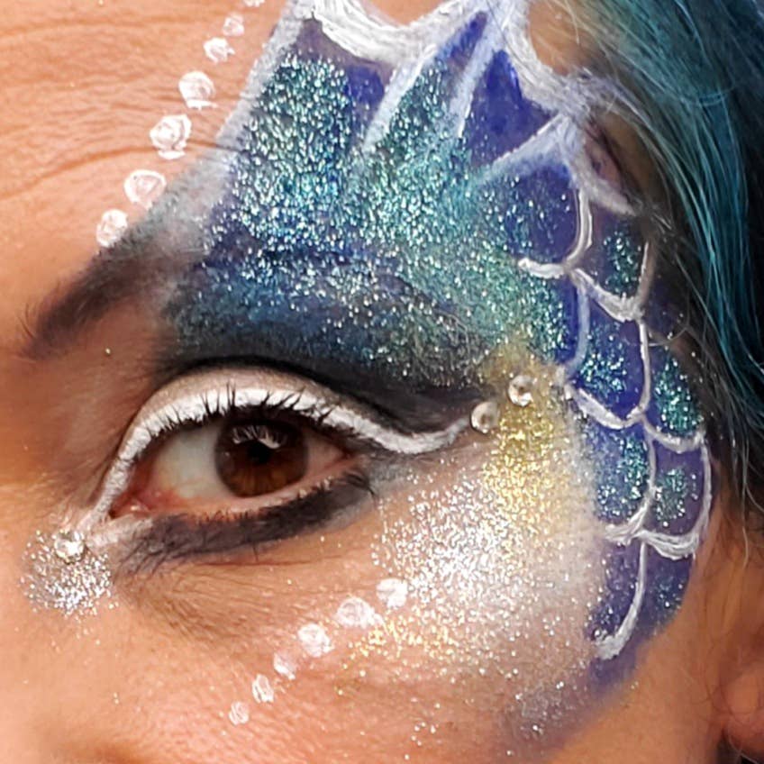 Close-up of a person with blue and white face paint resembling fish scales.