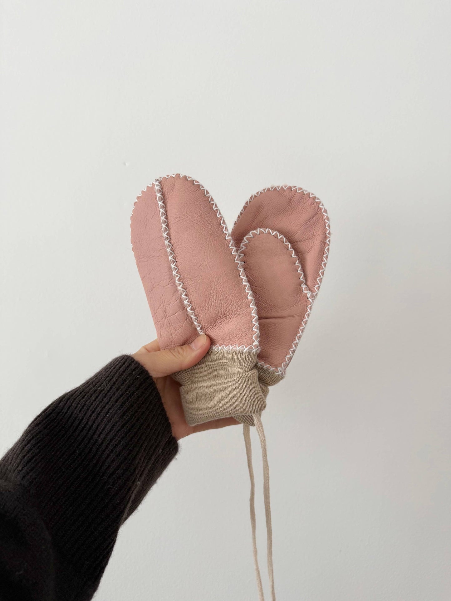 Pink mittens held by a hand against a white background
