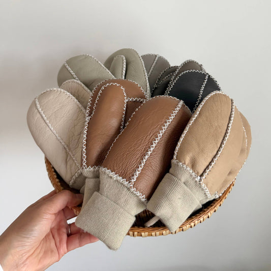 Set of leatheer mittens in various colors held in a hand against a white background