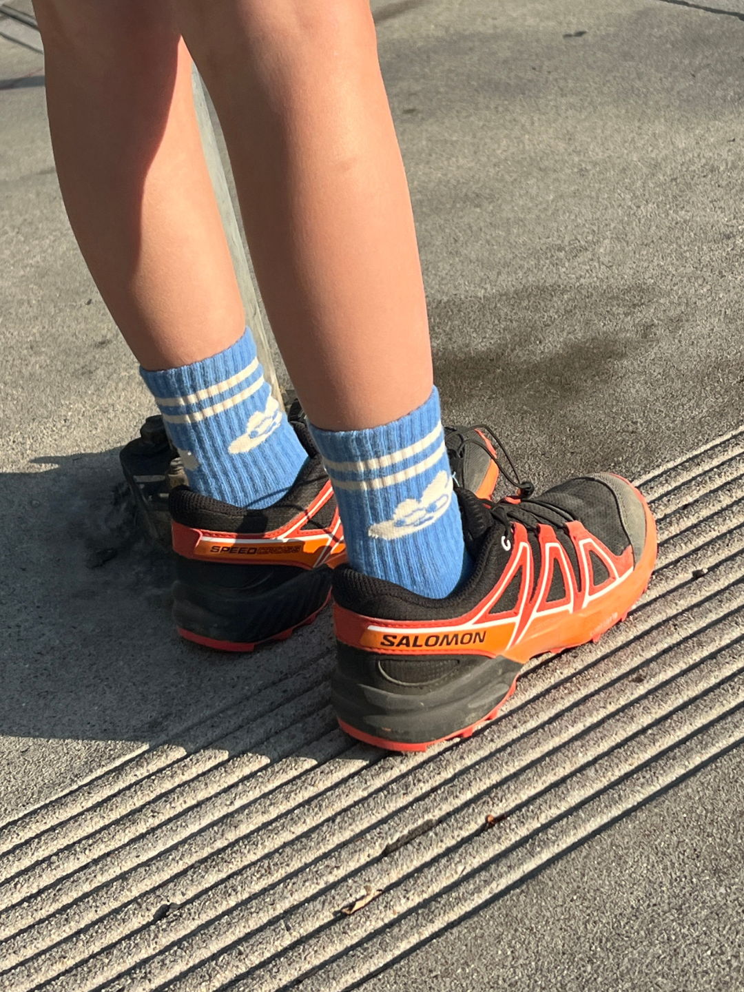 Person wearing blue socks with white stripes and Salomon running shoes on a pavement.