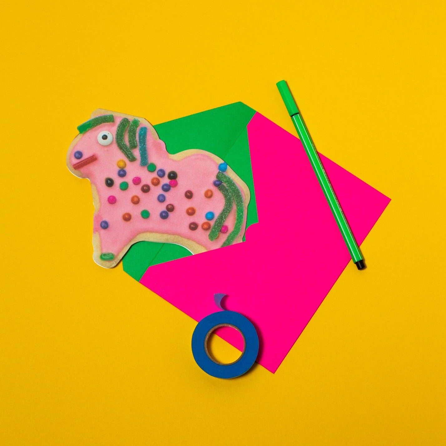 Colorful horse-shaped cookie with a green pen and pink paper on a yellow background