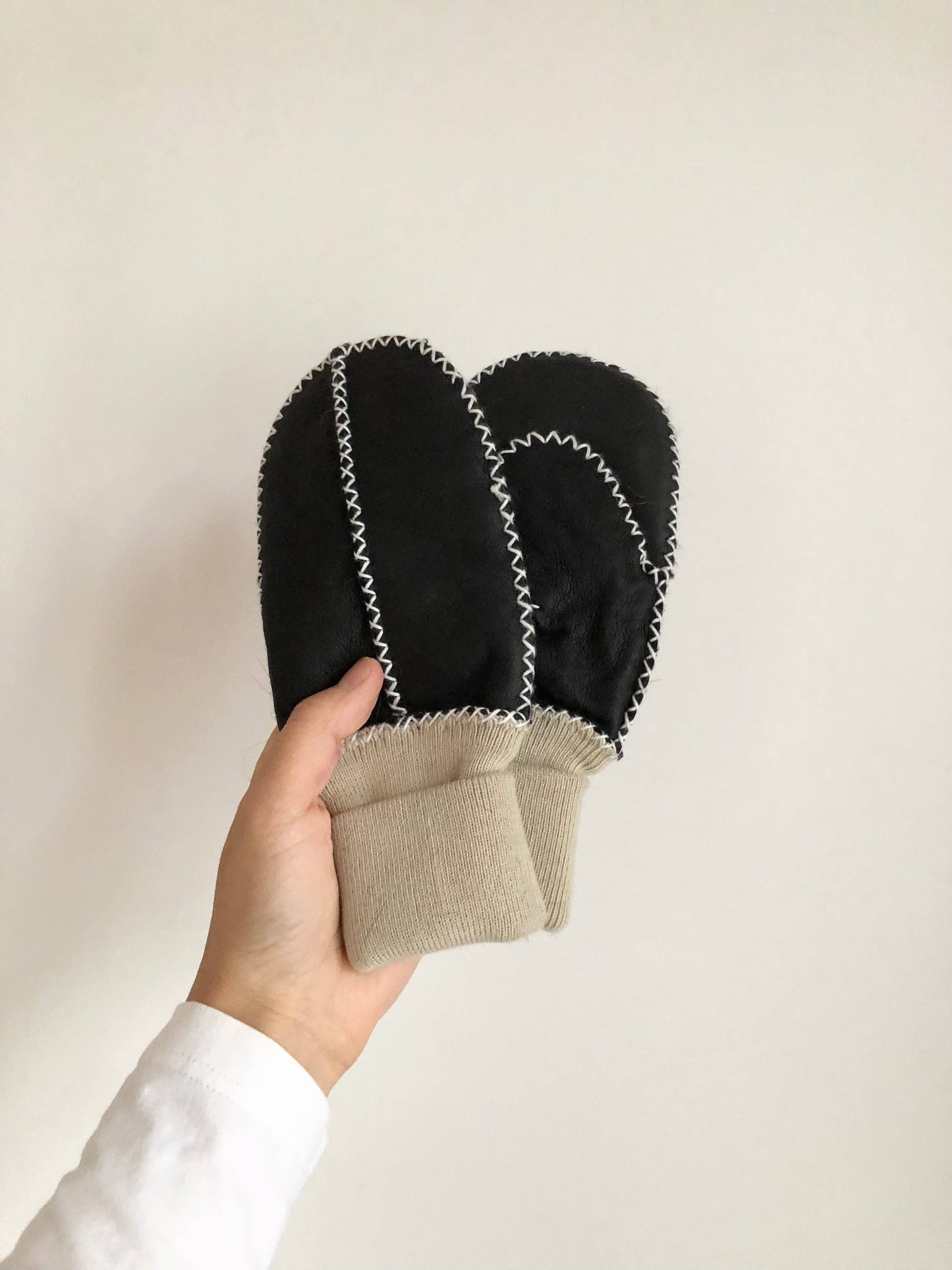 Hand holding a pair of blackl leather mittens against a white background