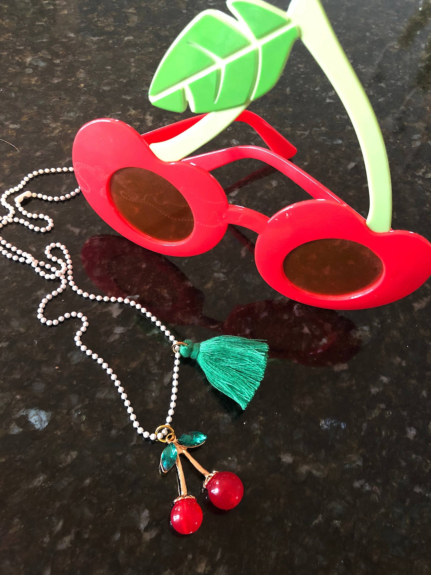 Red sunglasses with a cherry necklace on a dark surface