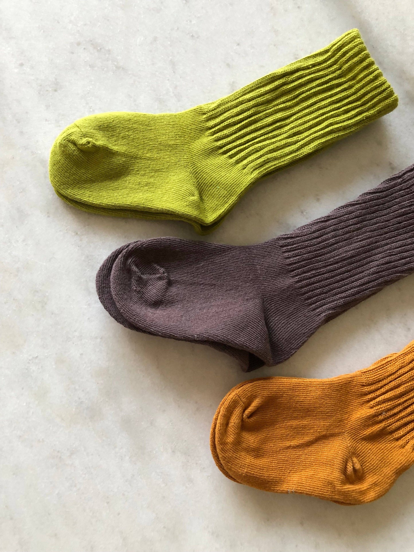 Three socks in green, purple, and orange on a textured surface