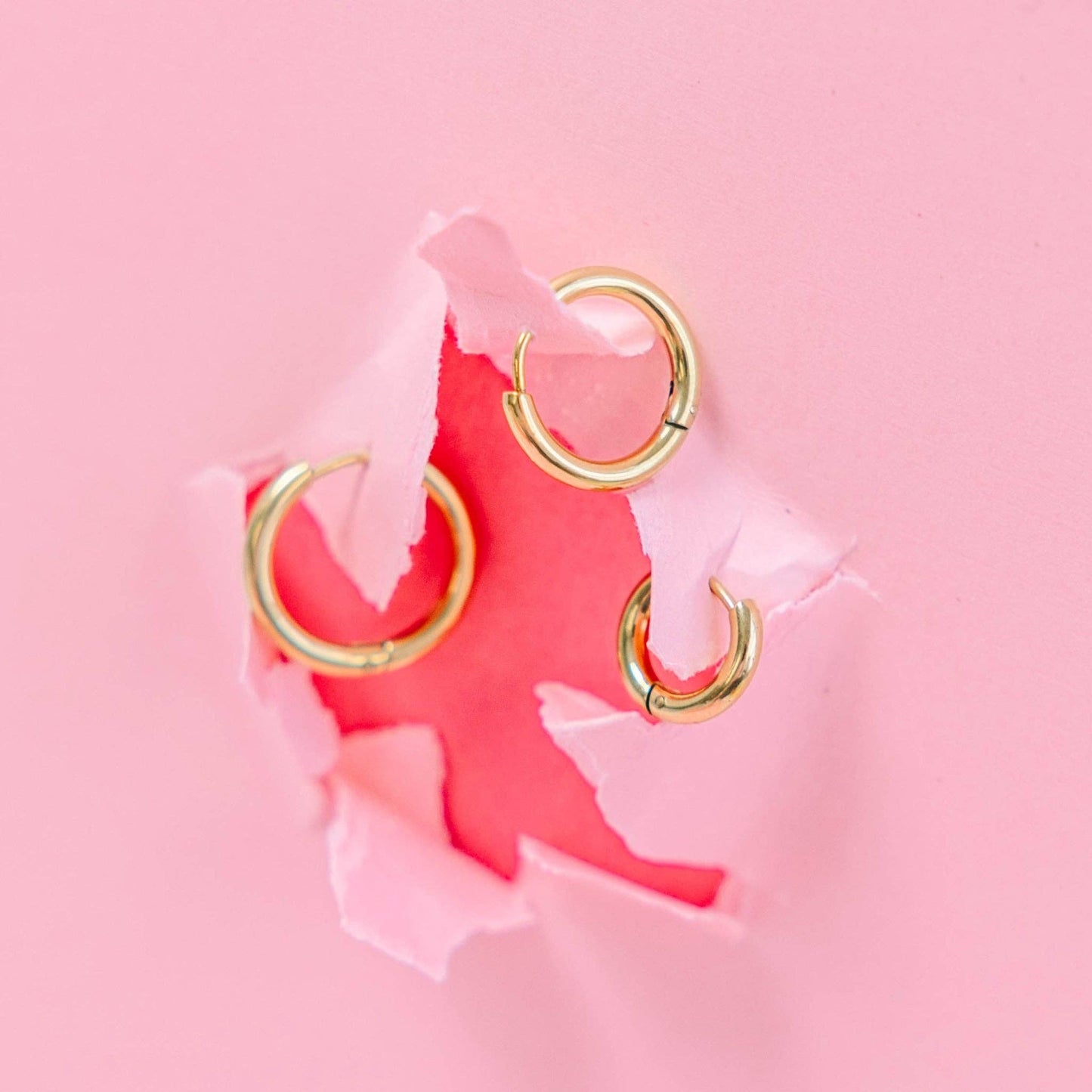 Gold hoop earrings on a pink background