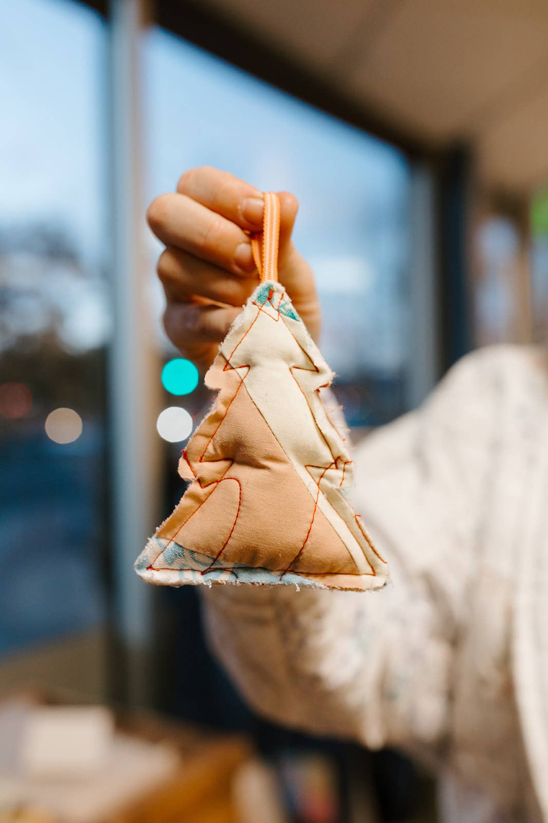 Hand holding a small fabric tree ornament with a blurred background