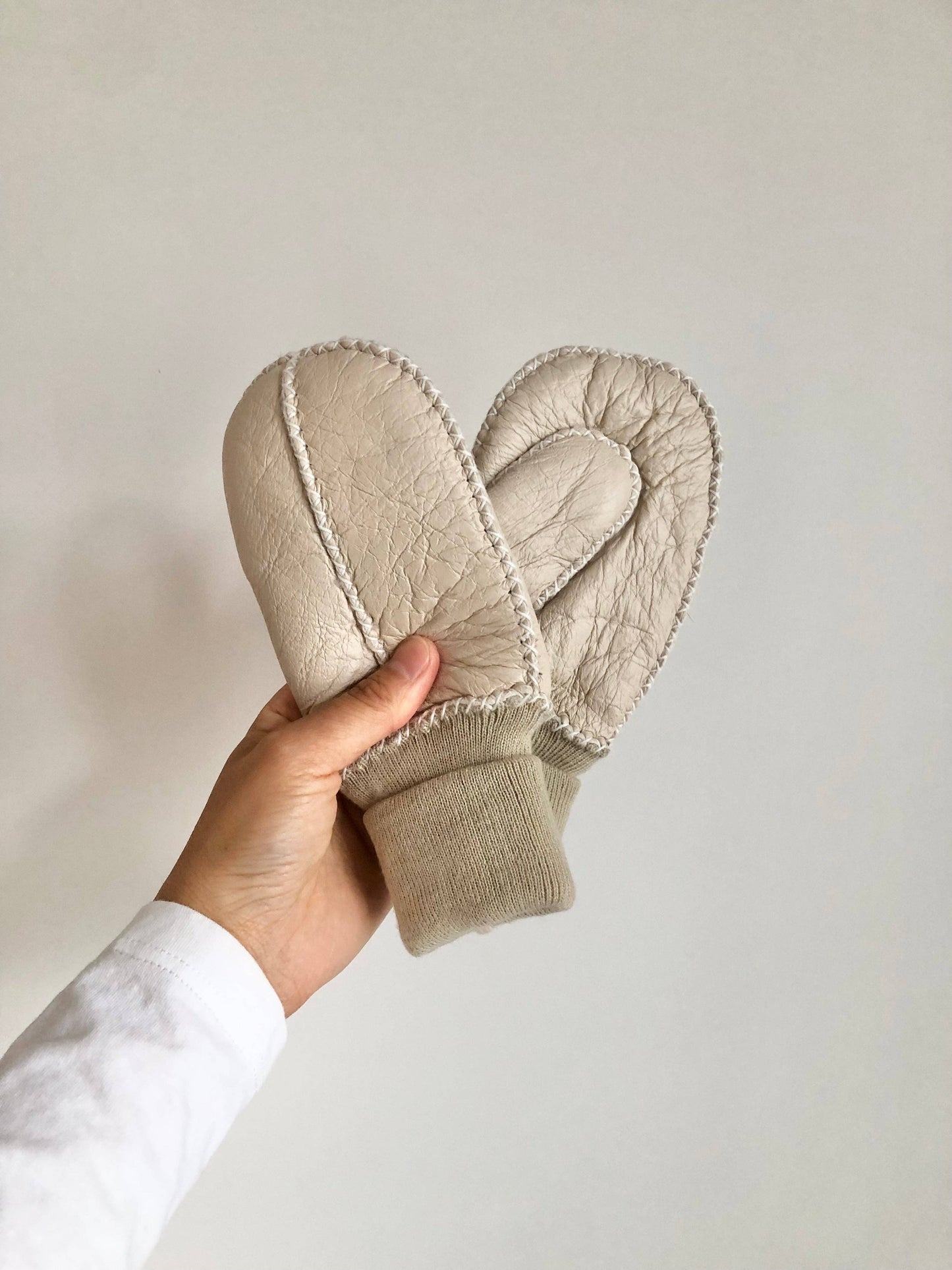 Beige mittens held by a hand against a plain background