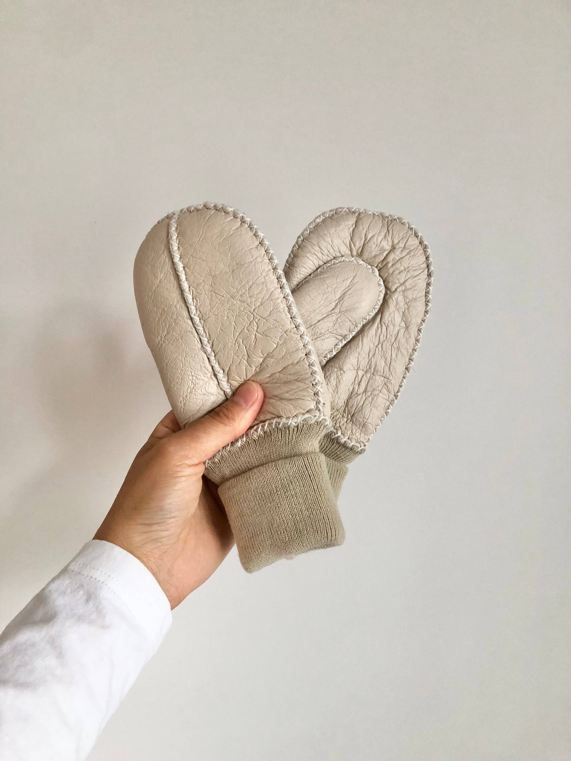 Beige mittens held by a hand against a plain background