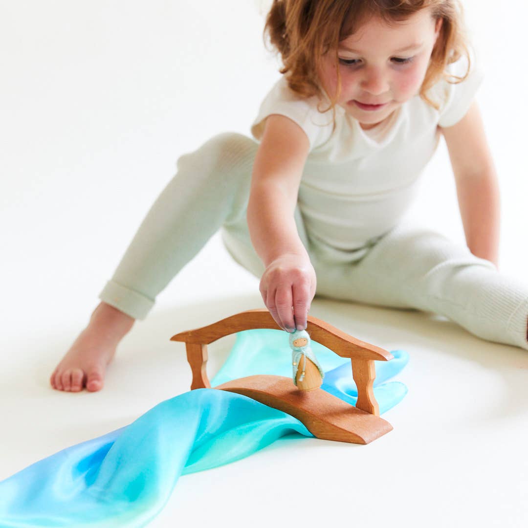 Child playing with a toy house and blue fabric on a white surface
