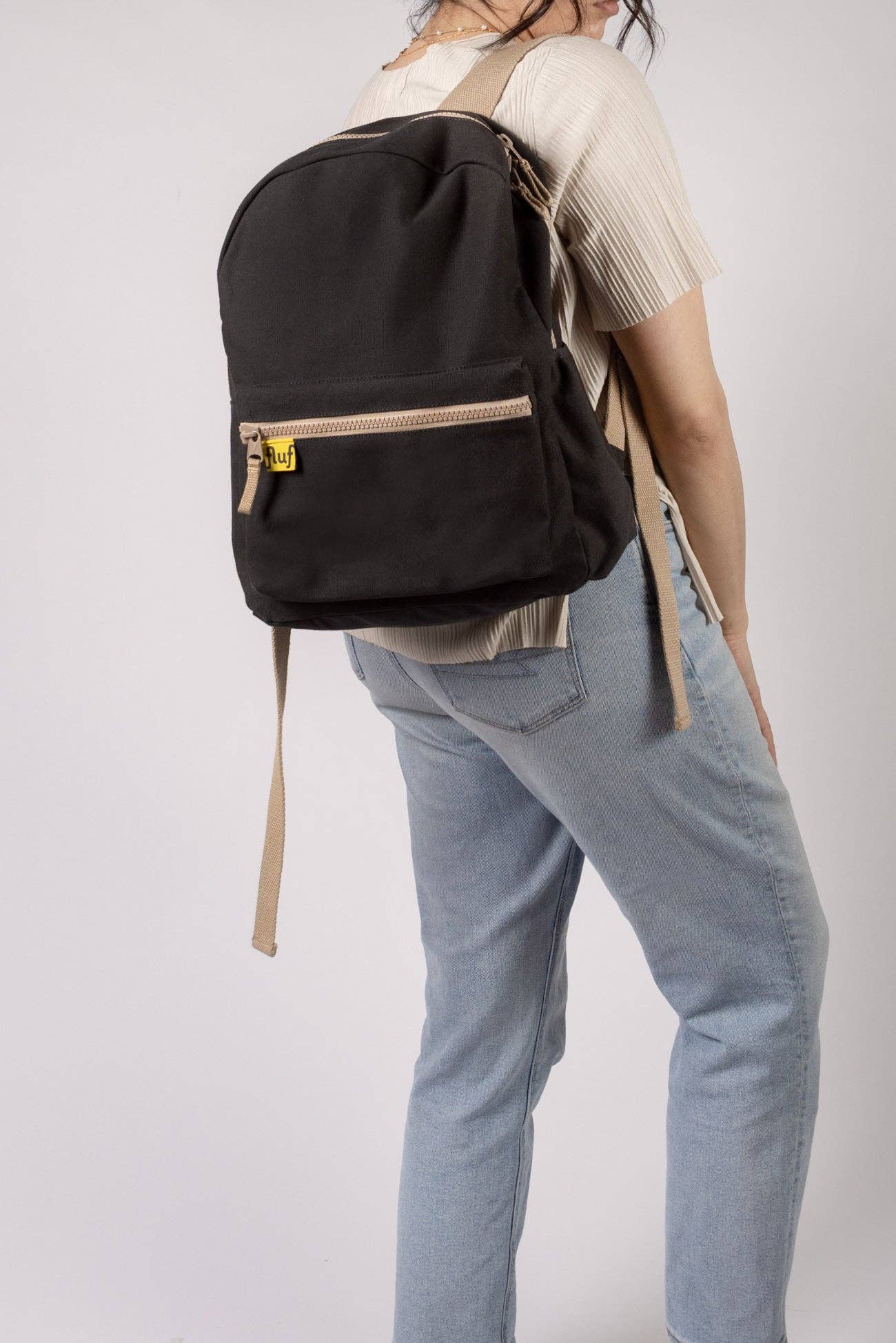 Person wearing a black backpack with a visible brand logo on a plain background