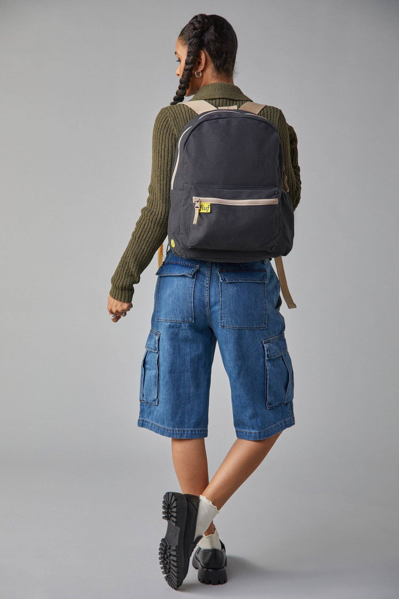 Person wearing a dark blue backpack and denim shorts on a gray background