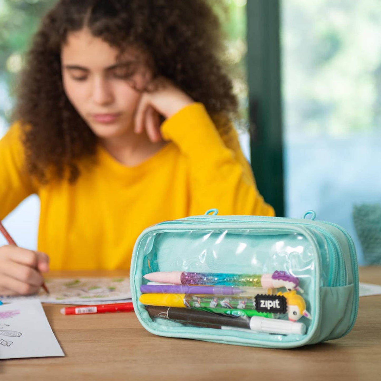 Person sitting at a table with a teal pencil case containing stationery items.