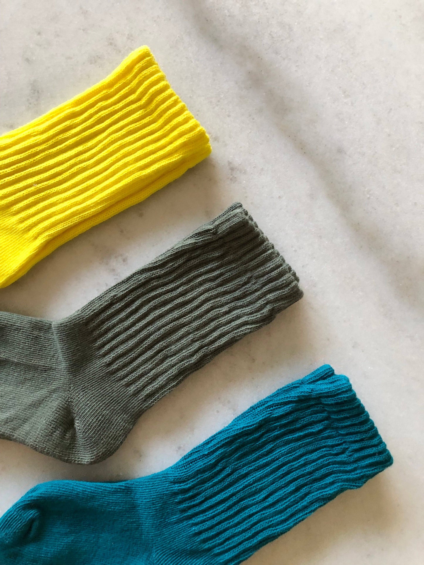 Three socks in yellow, green, and blue on a light fabric background