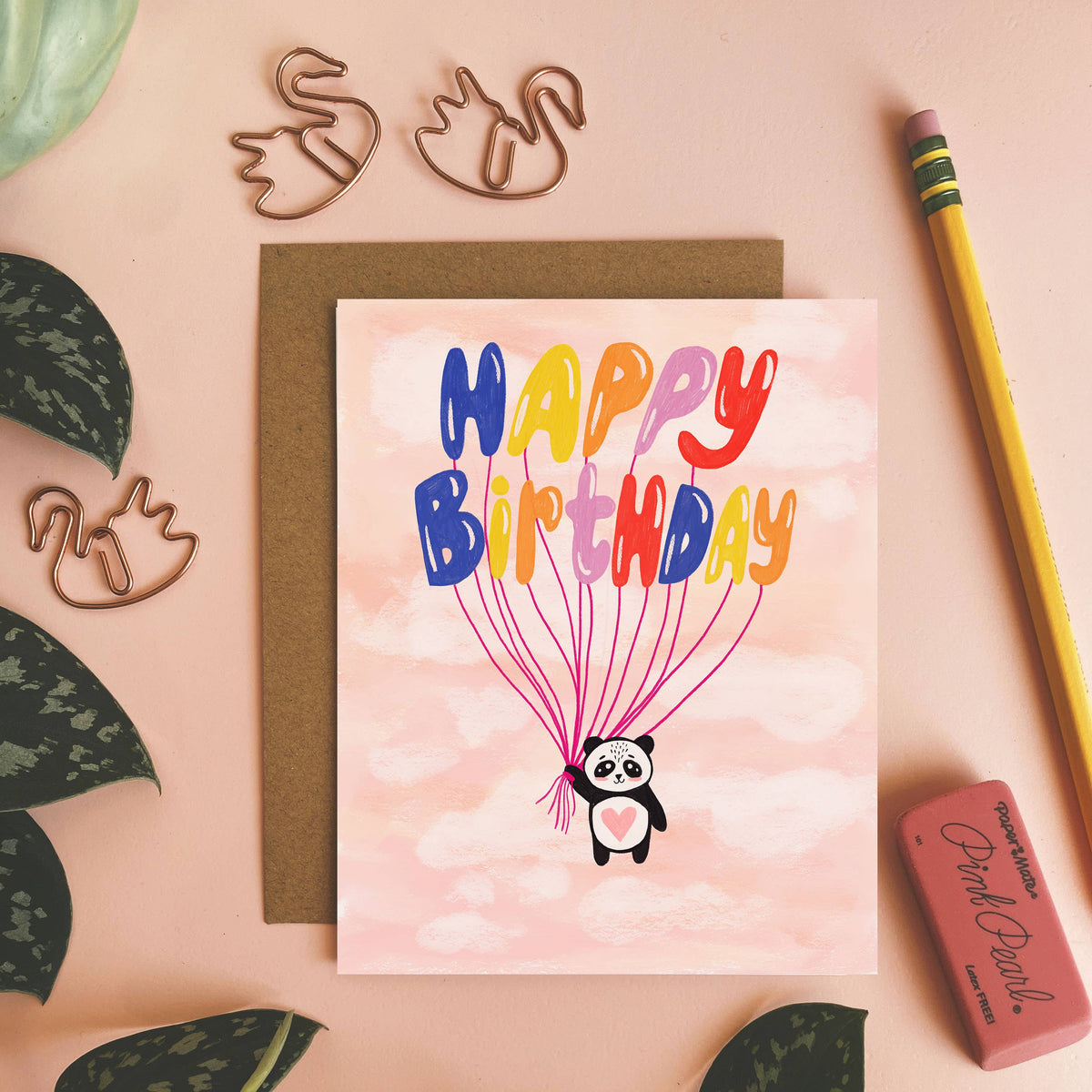 Happy Birthday card with panda and balloons on a pink background, surrounded by decorative items.