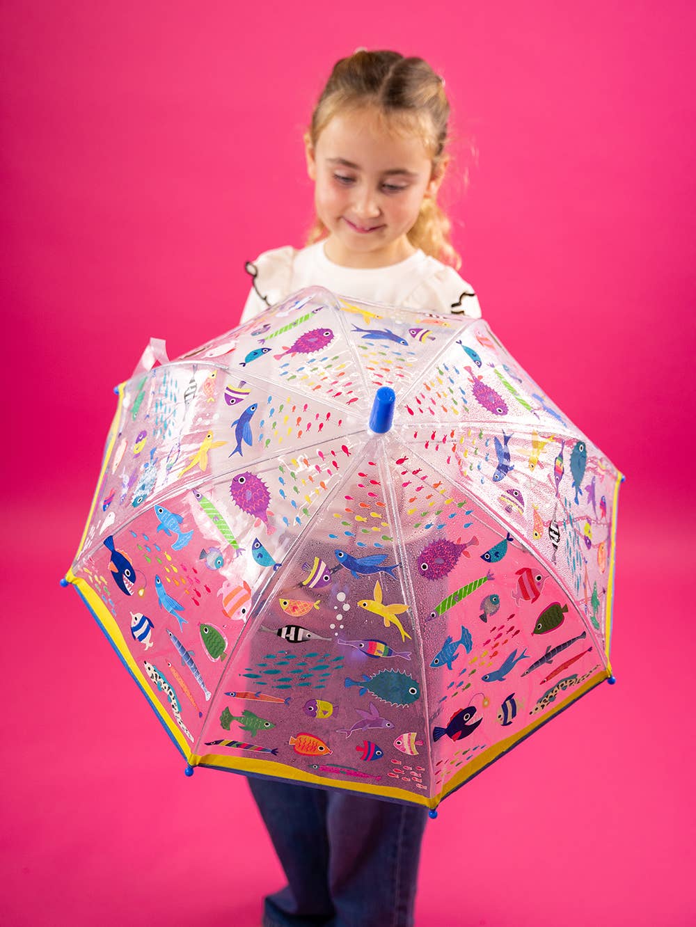 Child holding a colorful umbrella with animal patterns against a pink background