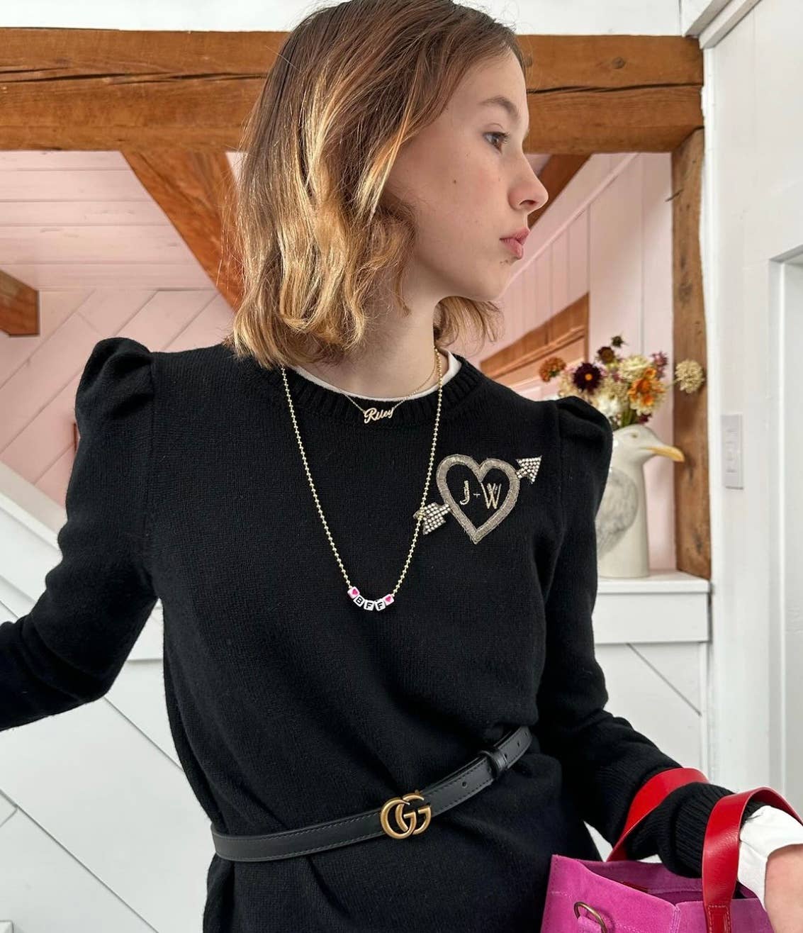 Woman wearing a black sweater with a heart-shaped brooch, standing indoors.