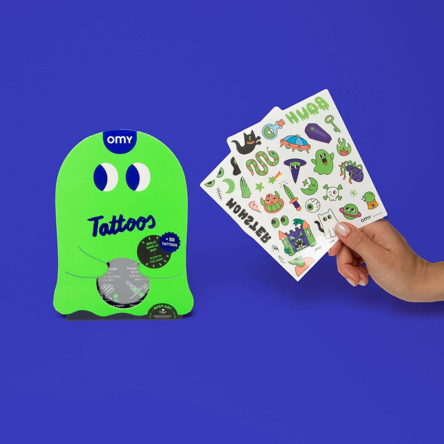 Green package of OMY tattoos with a hand holding a sheet of stickers against a blue background