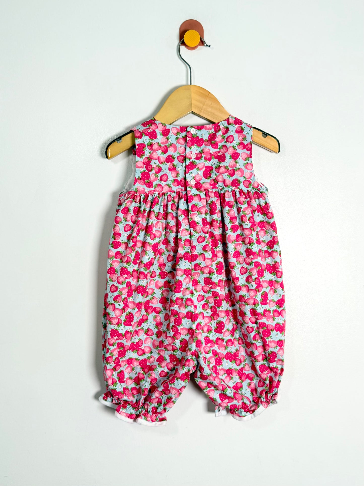 Floral-patterned baby romper on a wooden hanger against a white background