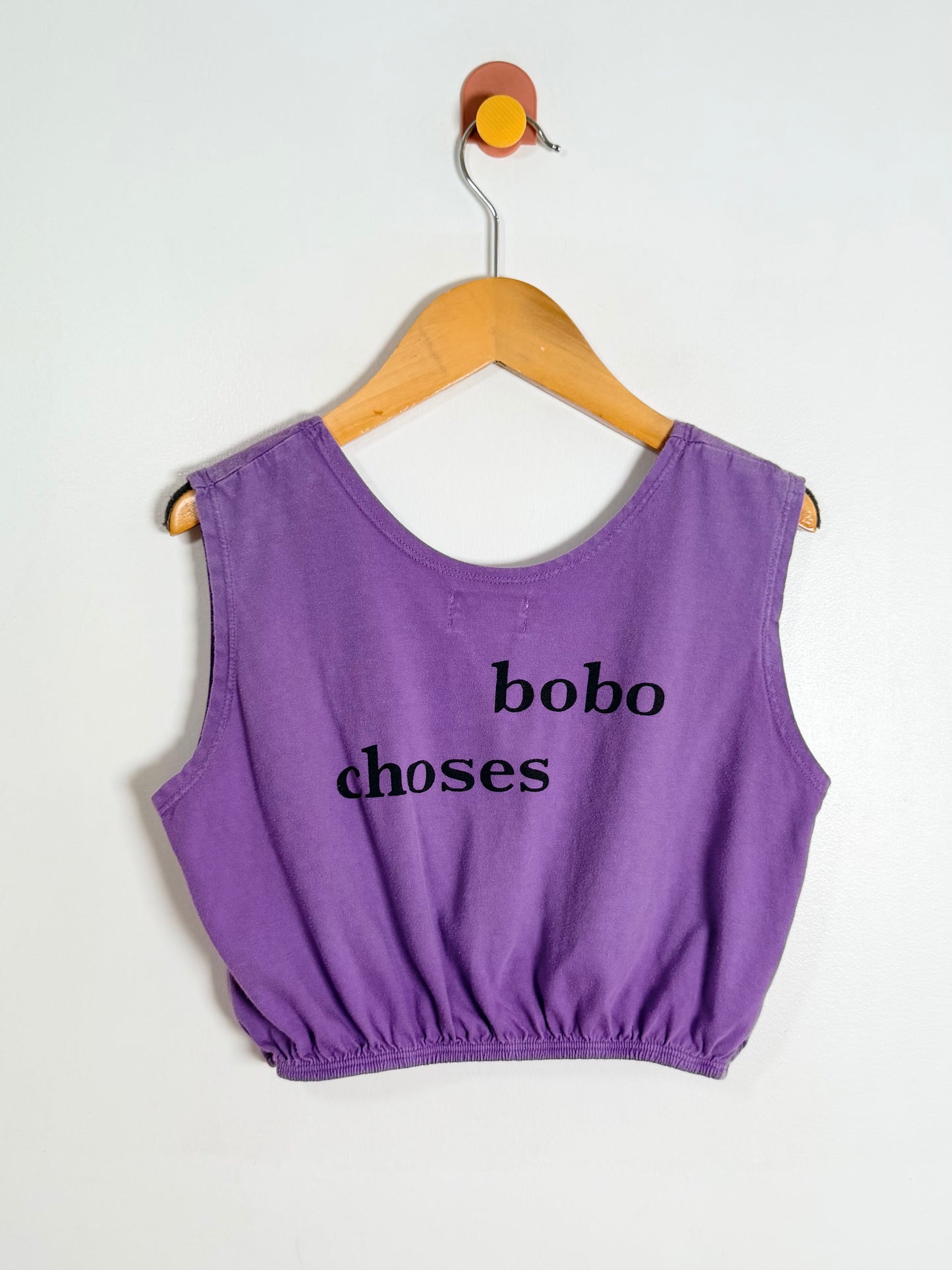 Purple tank top with 'bobochoses' text on a wooden hanger against a white background