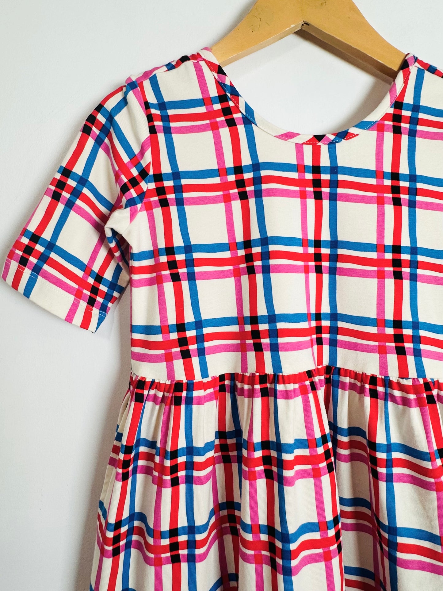 Plaid dress with red, blue, and pink pattern on a hanger against a white background