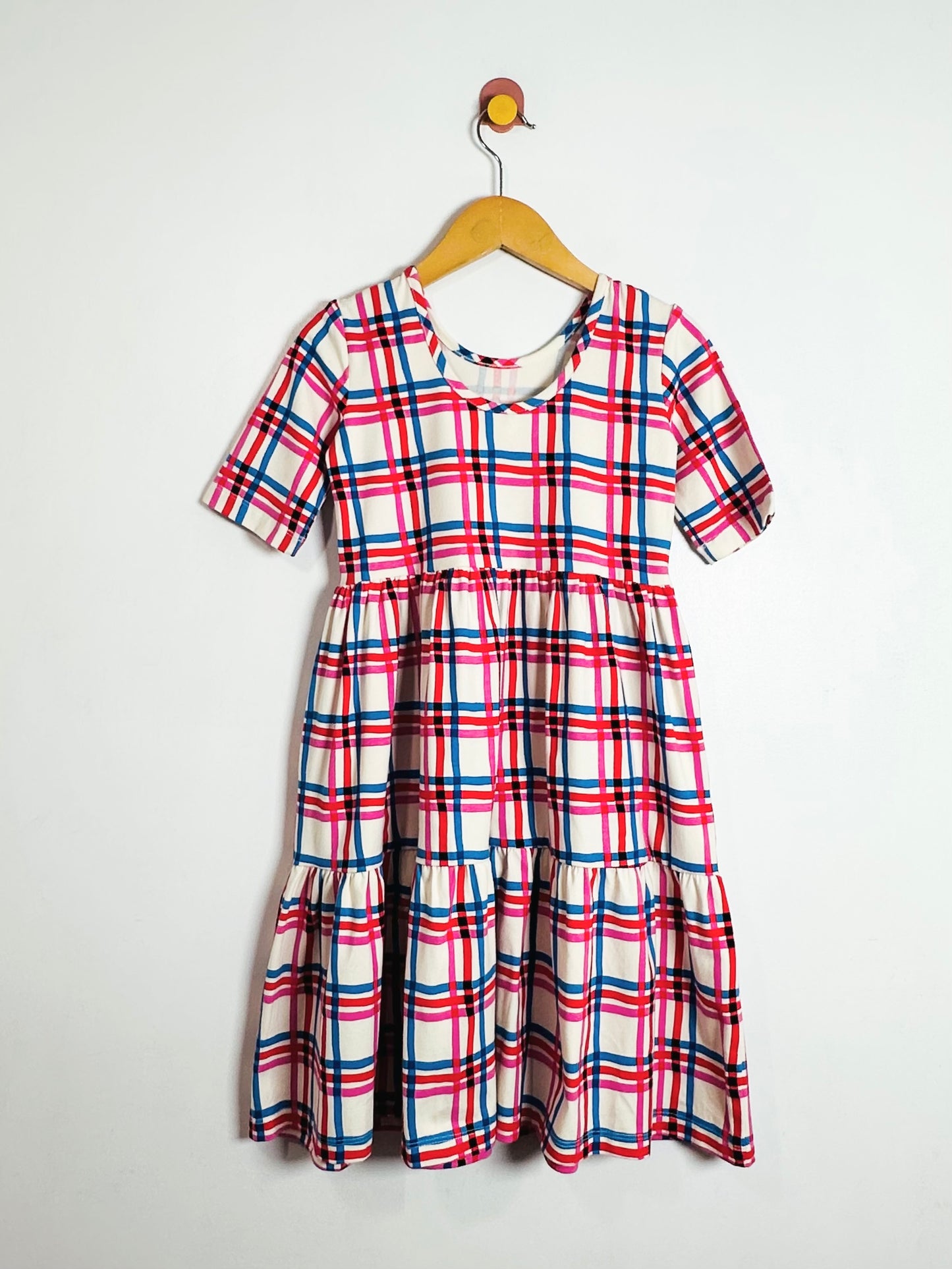 Plaid dress with red, white, and blue pattern on a hanger against a white background