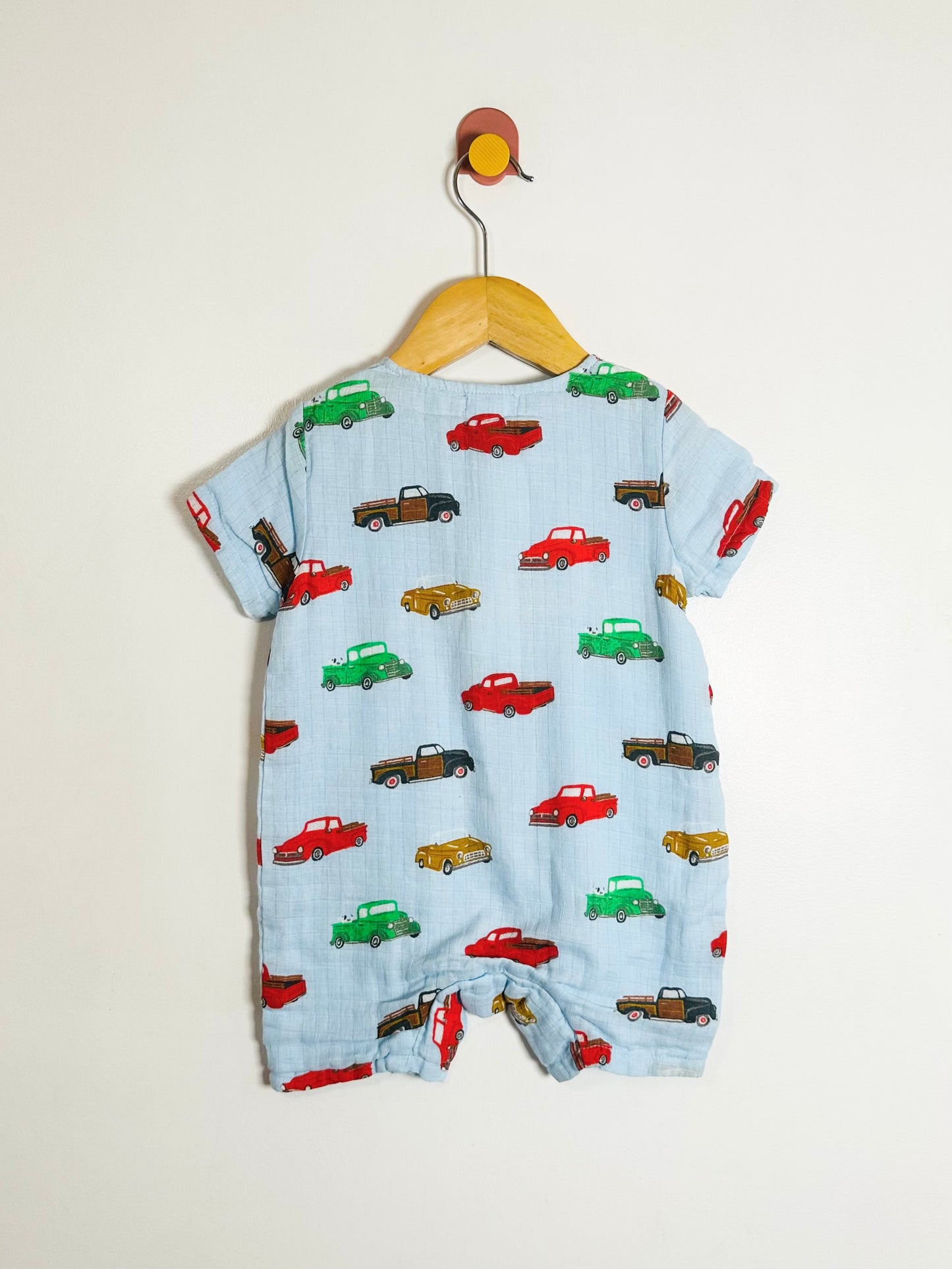 Baby romper with car pattern on a hanger against a beige background