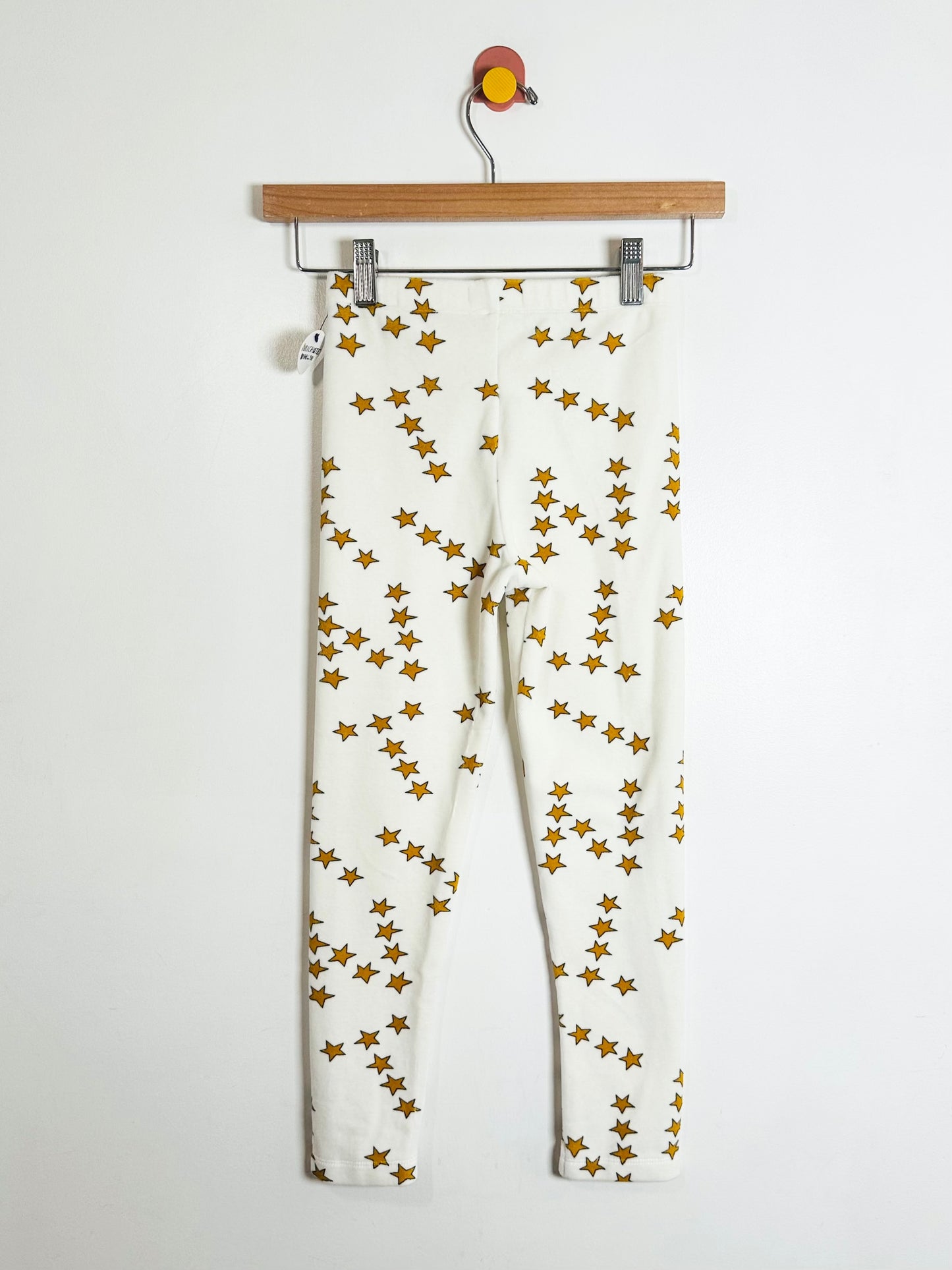 White pants with gold star pattern on a hanger against a white background