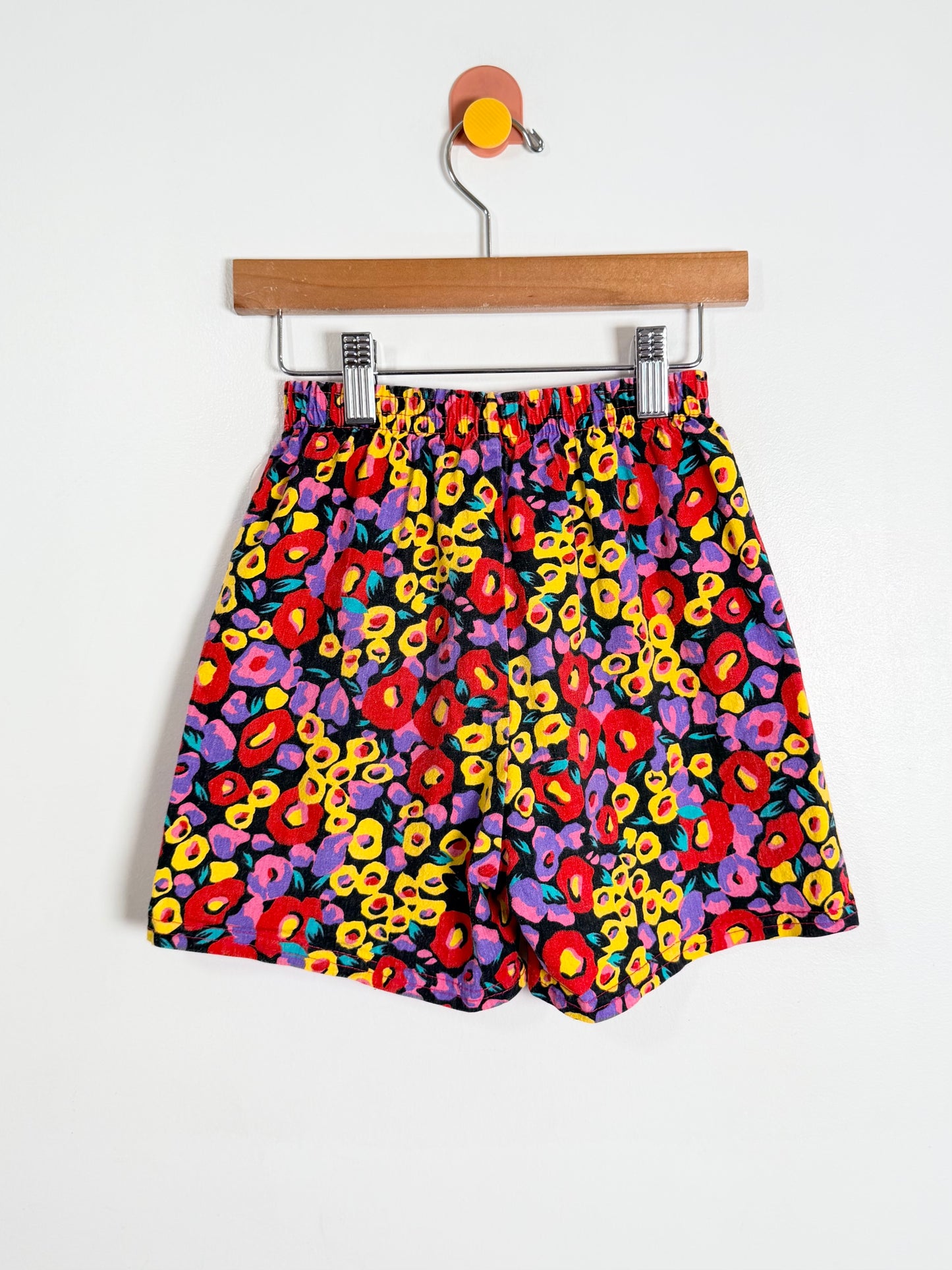 Colorful floral-patterned shorts on a hanger against a white background