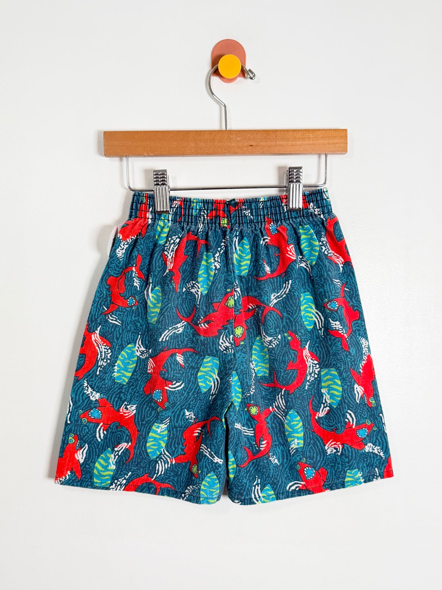 Children's shorts with red and green pattern on a hanger against a white background