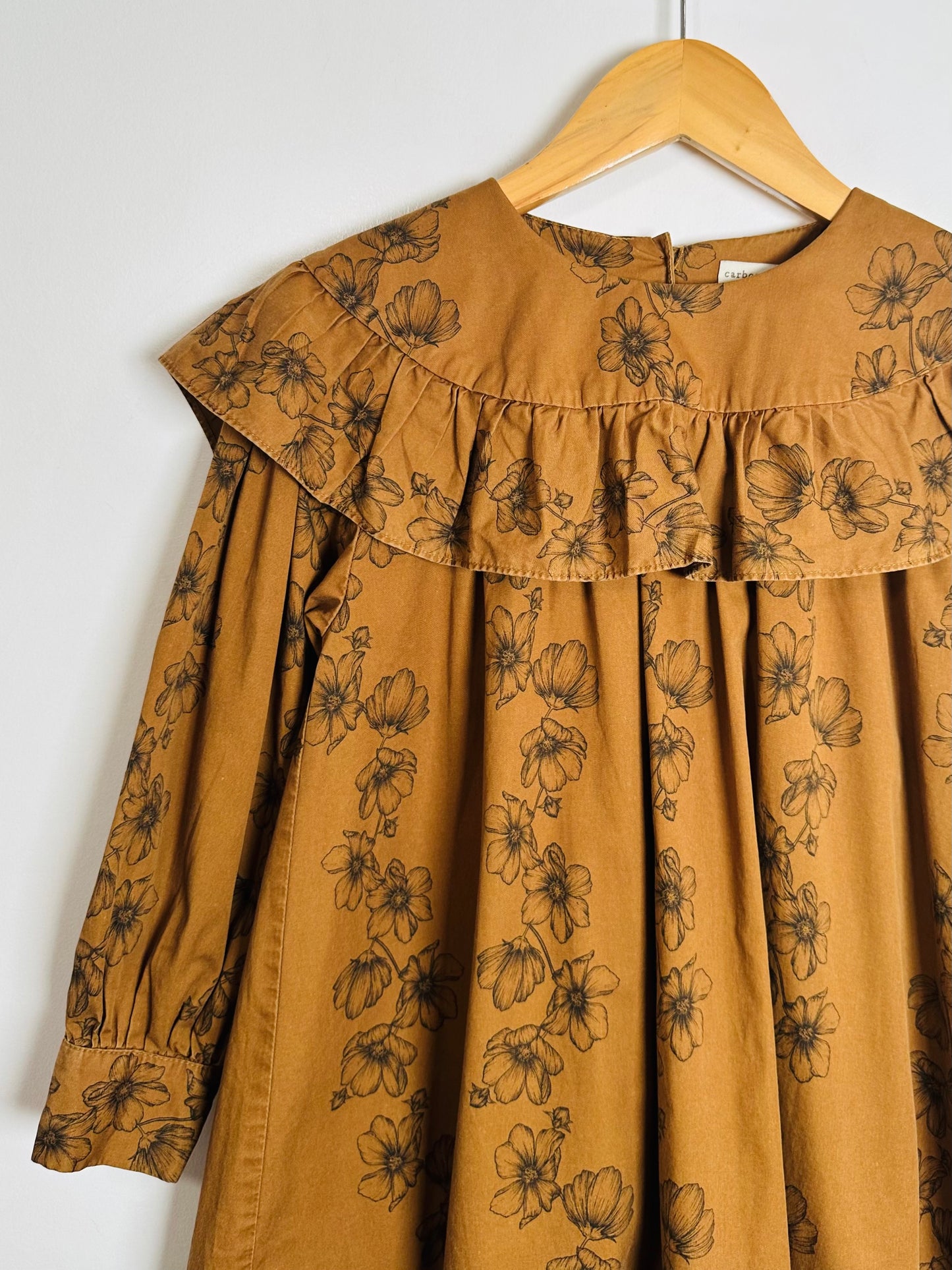 Brown dress with floral patterns on a hanger against a white background