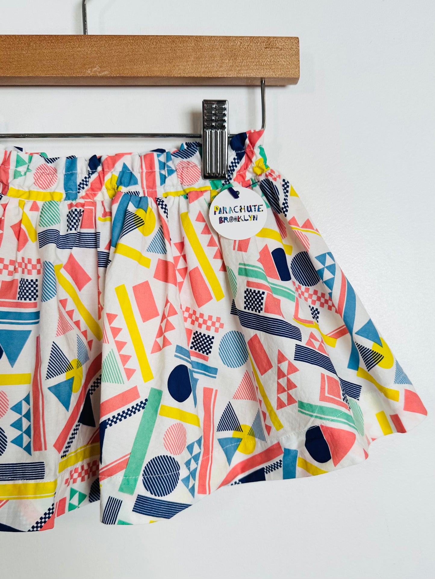 Colorful geometric-patterned pants hanging on a wooden hanger against a white background