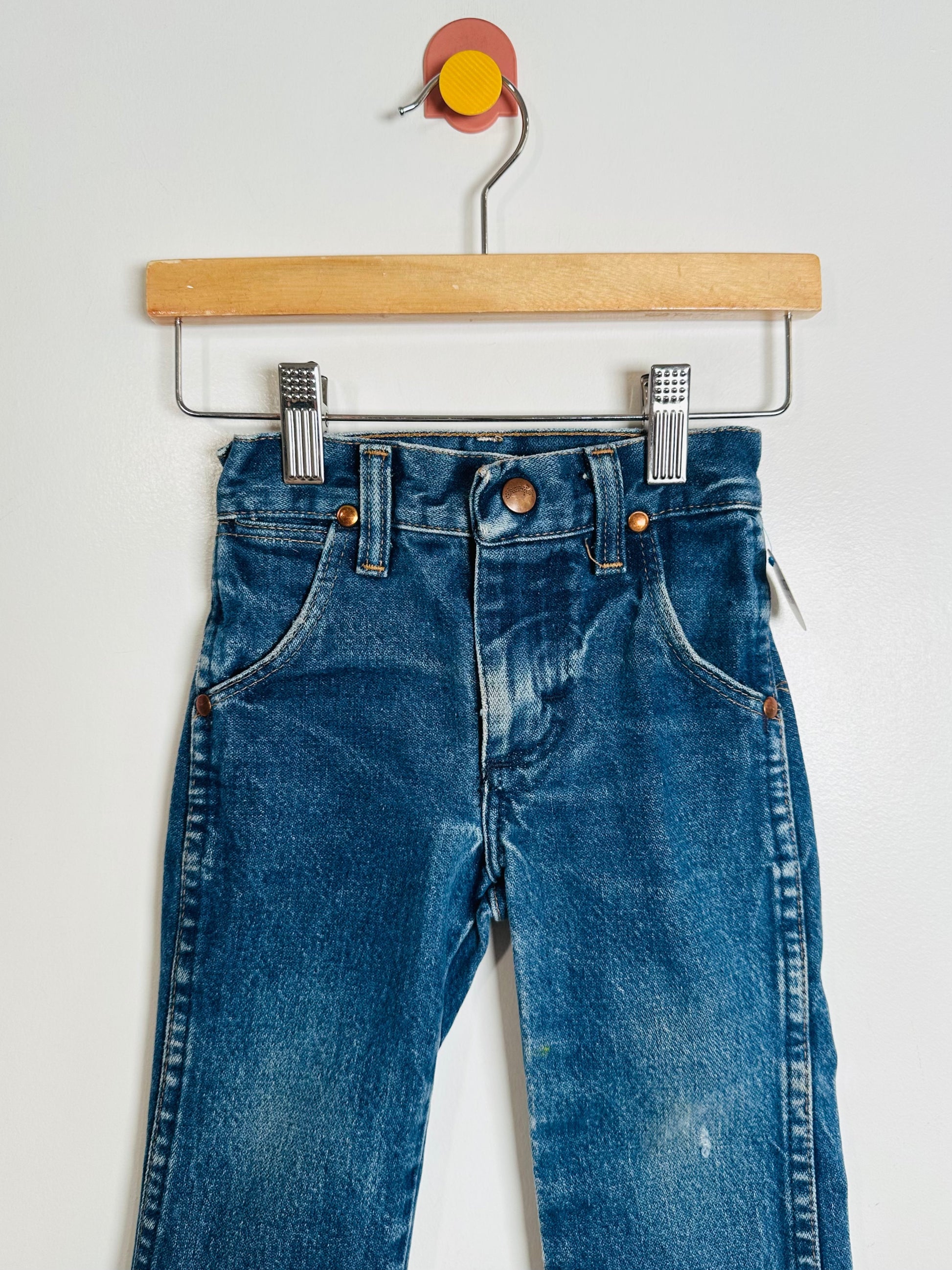 Blue jeans hanging on a wooden hanger against a white background