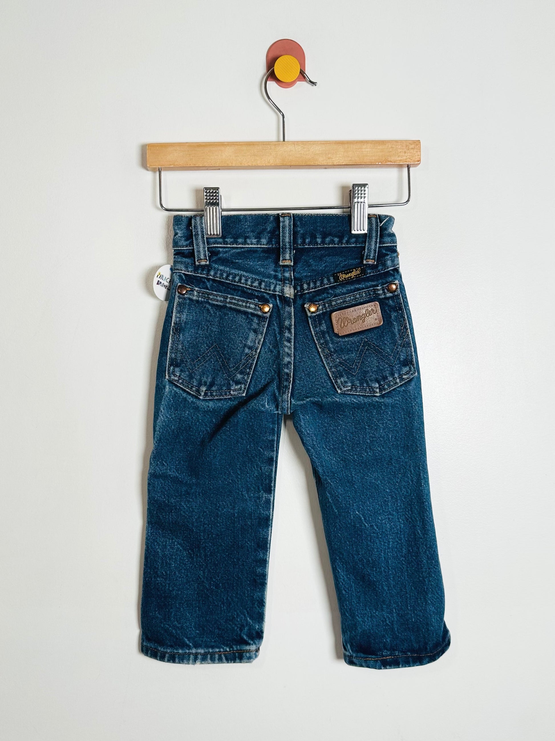 Pair of blue jeans hanging on a wooden hanger against a white background