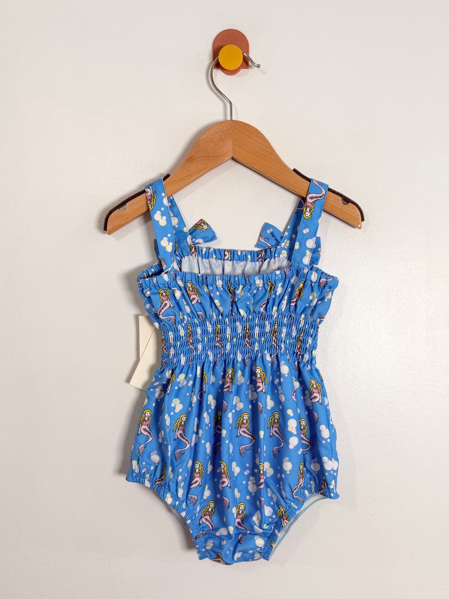 Blue children's romper with animal print on a hanger against a white background