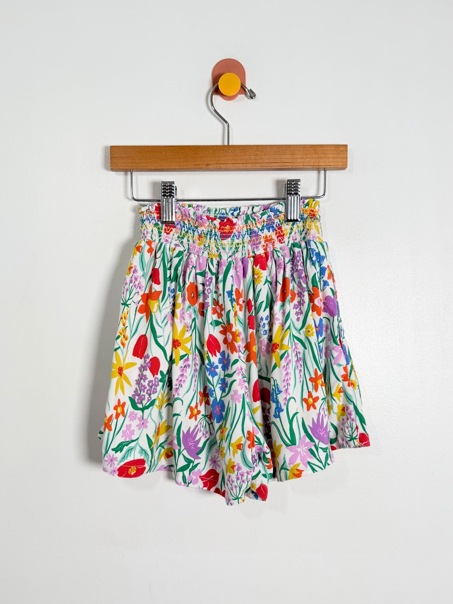 Colorful floral shorts on a wooden hanger against a white background