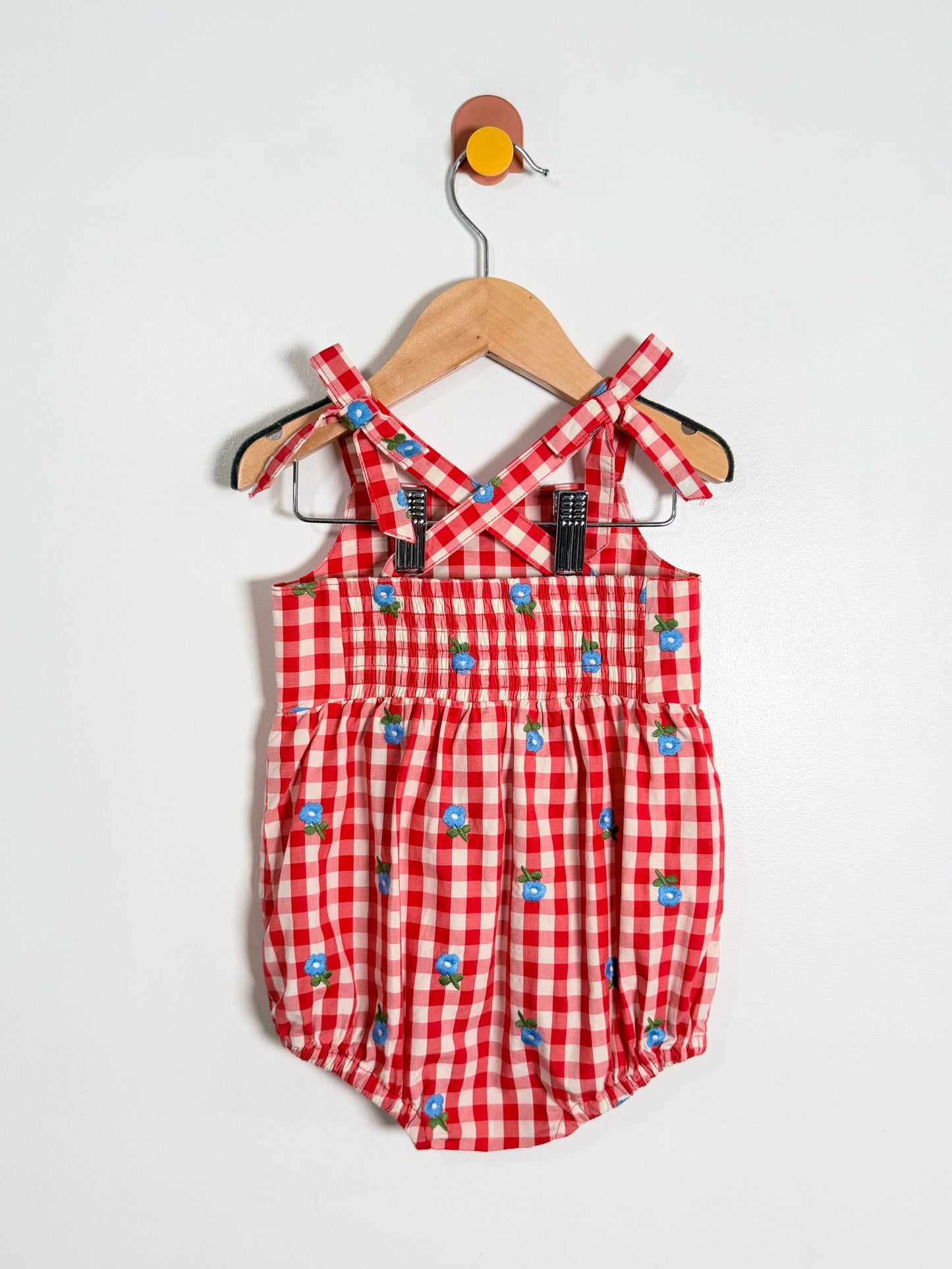 Red checkered romper with blue floral patterns on a hanger against a white background