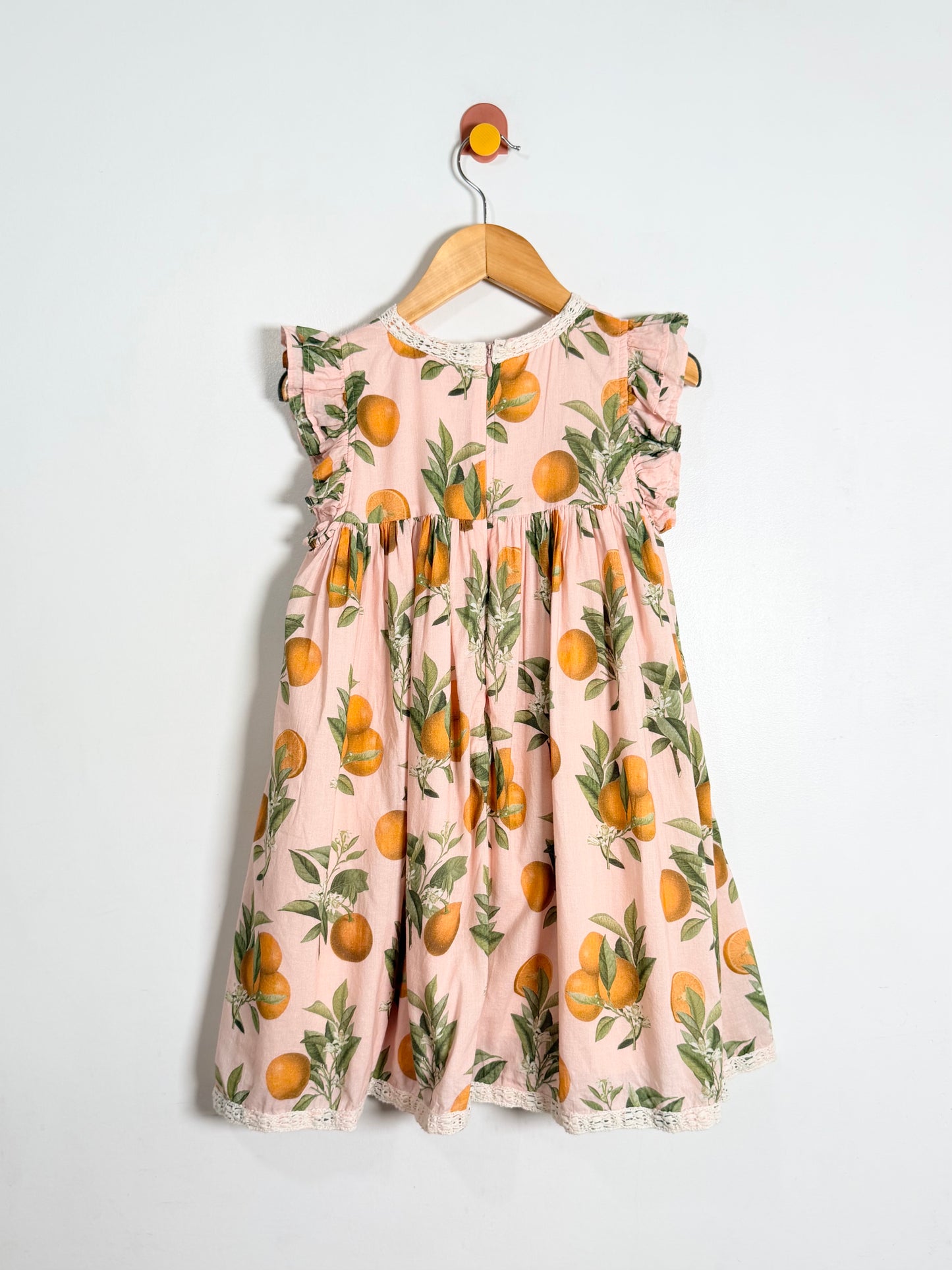 Children's dress with orange pattern on a hanger against a white background
