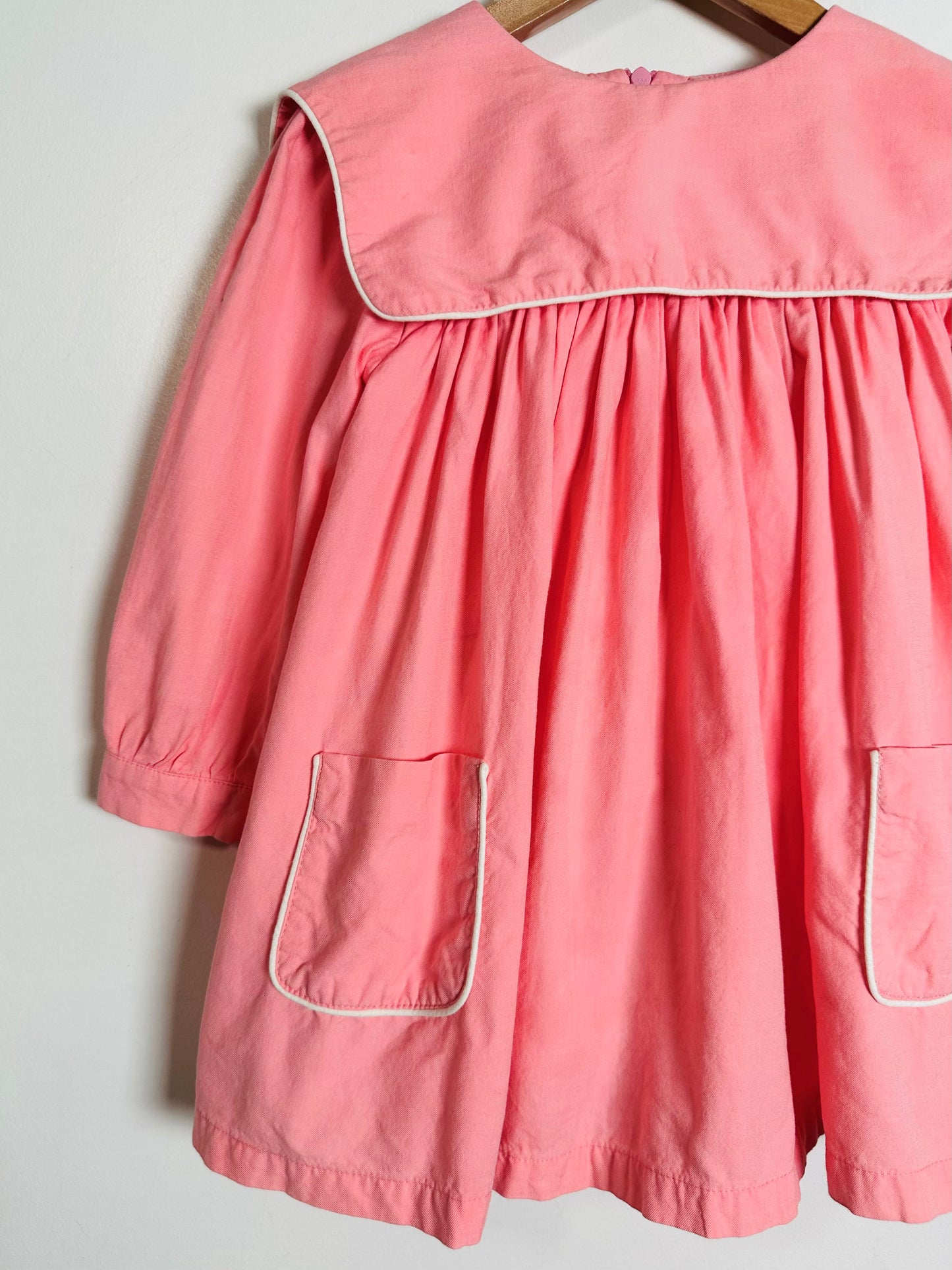 Pink dress with white trim on a wooden hanger against a light gray background